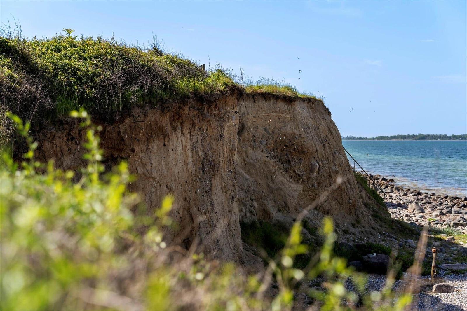 Steep coastal cliff with greenery and view of the sea.