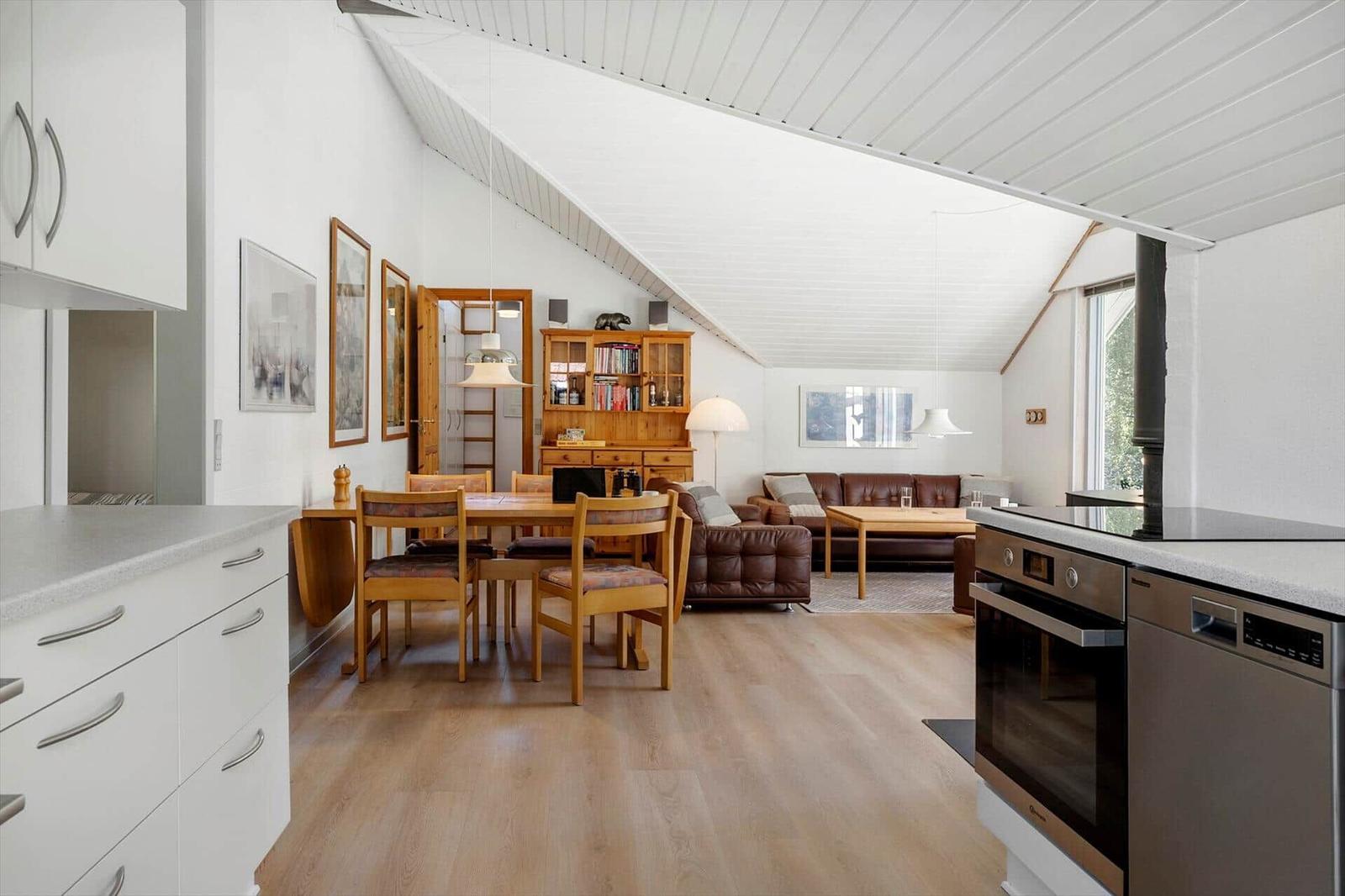 Open space with kitchenette, dining table, and living area under sloped ceilings.