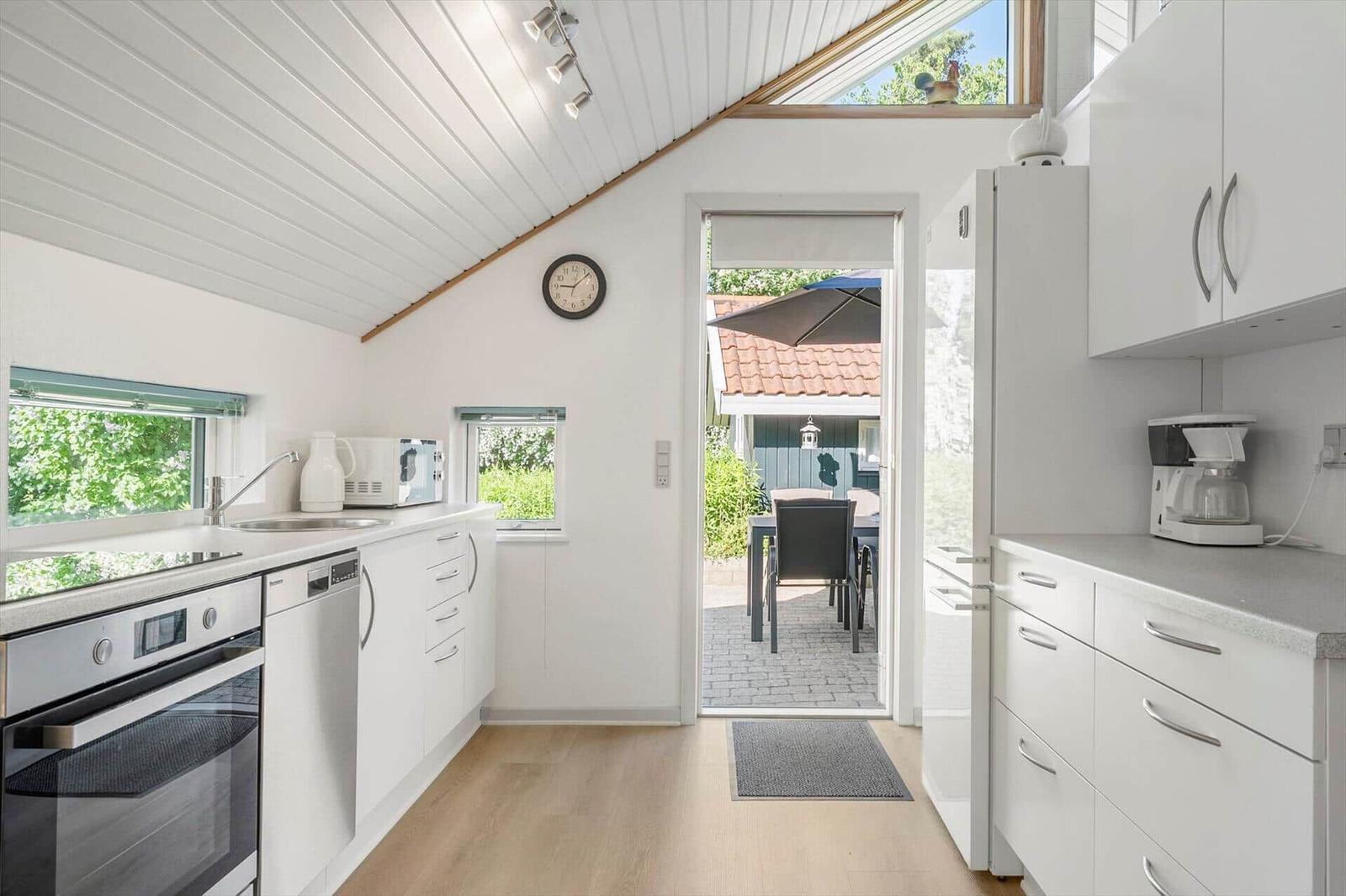 Kitchen with white cabinetry, oven, and refrigerator. Passage to terrace with table and chairs.