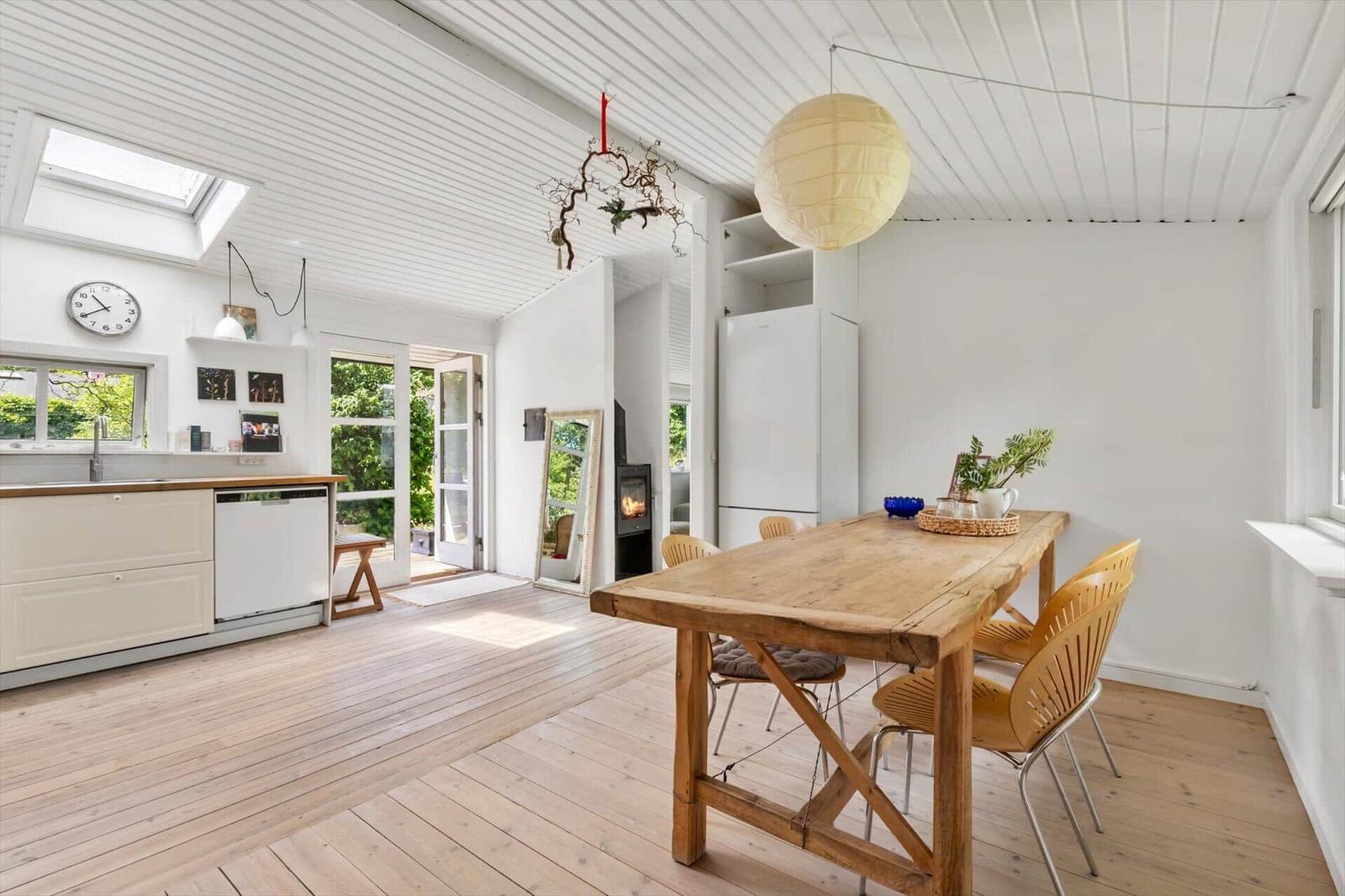 Dining area with wooden table and chairs. Kitchen and living area are open. Ceiling with shingles.