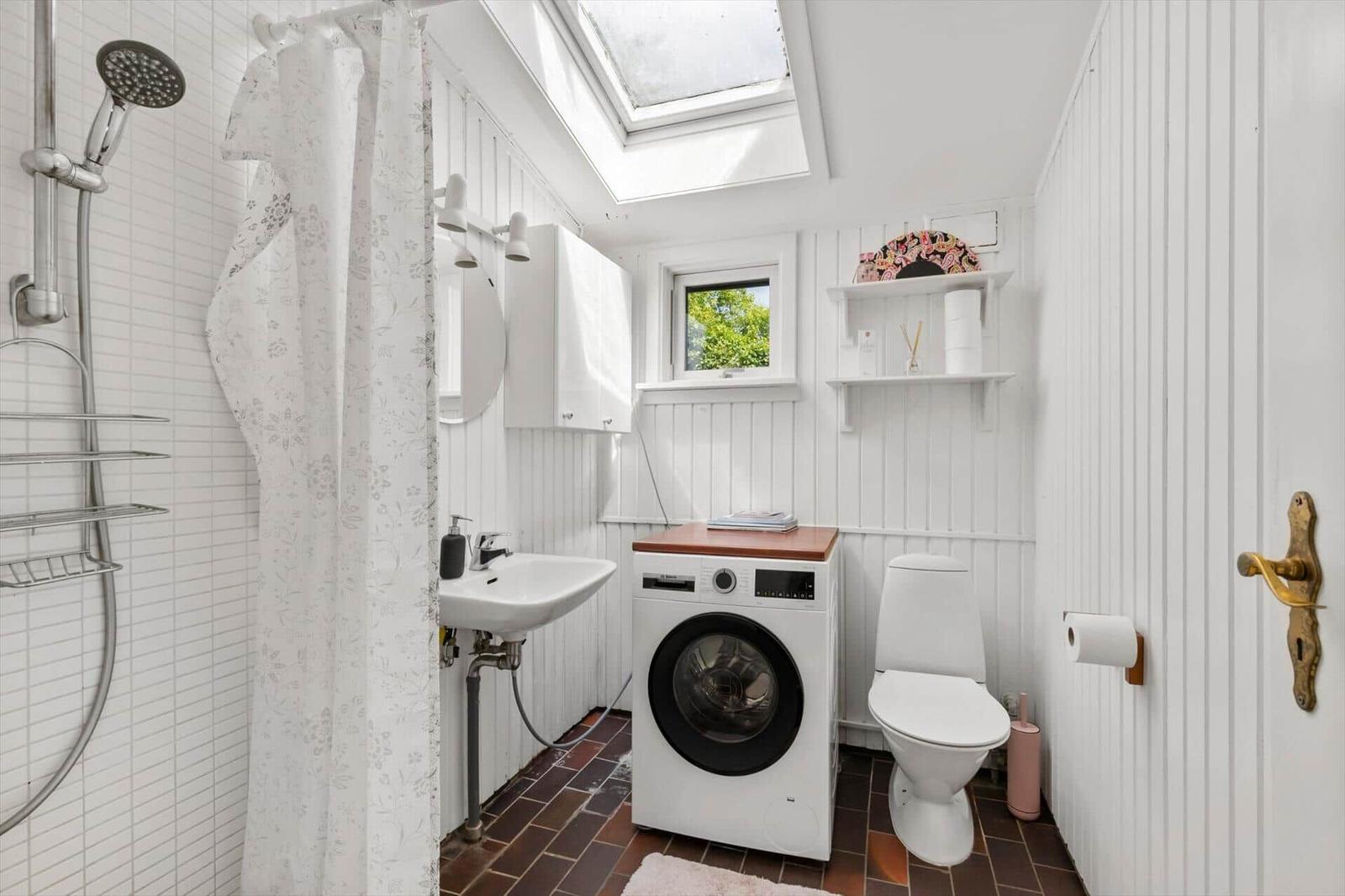 Bathroom with shower, washing machine, and toilet. Window and skylight provide daylight.