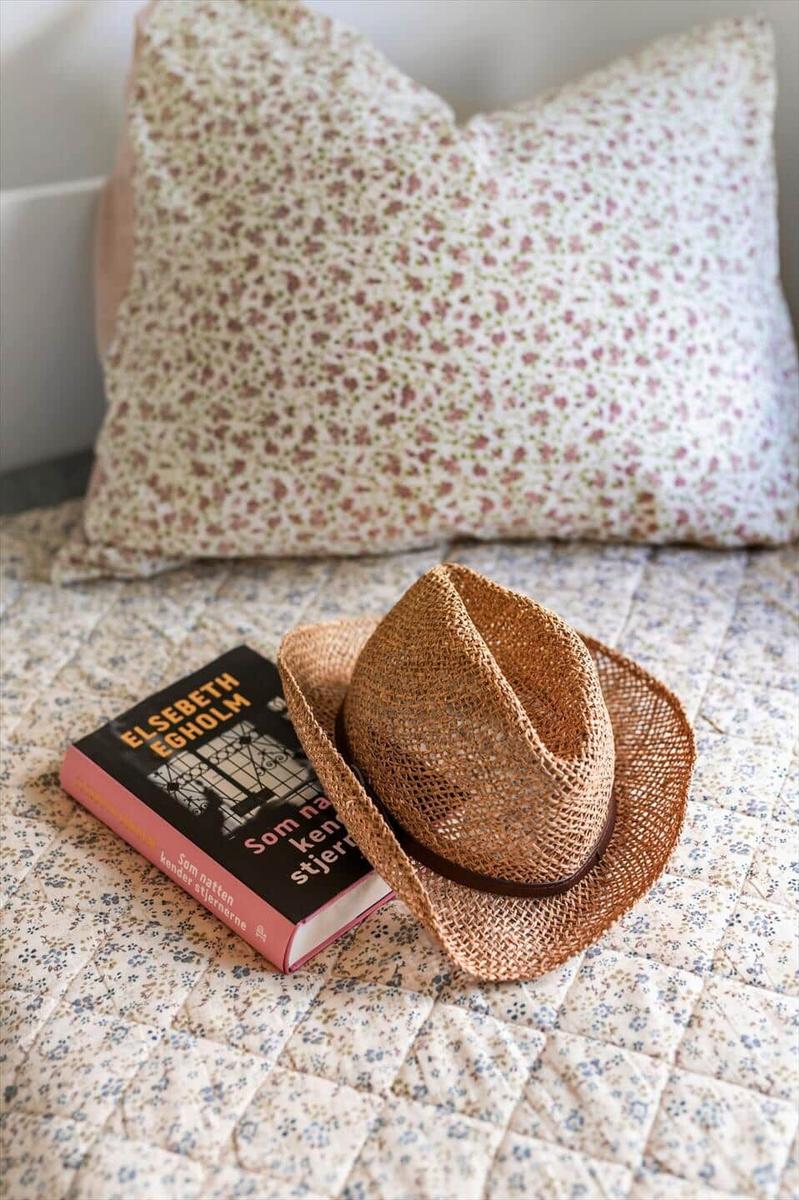 A straw hat and a book rest on a patterned bedspread.
