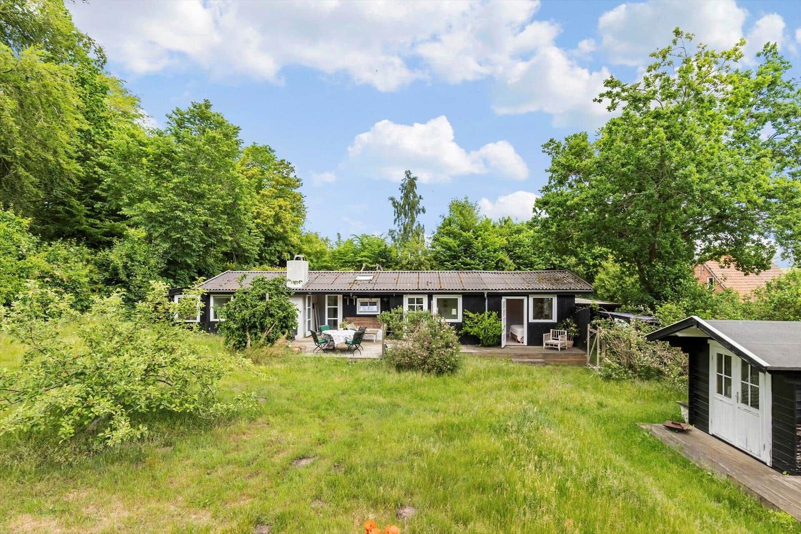 Black house with terrace and garden, surrounded by trees under blue sky.
