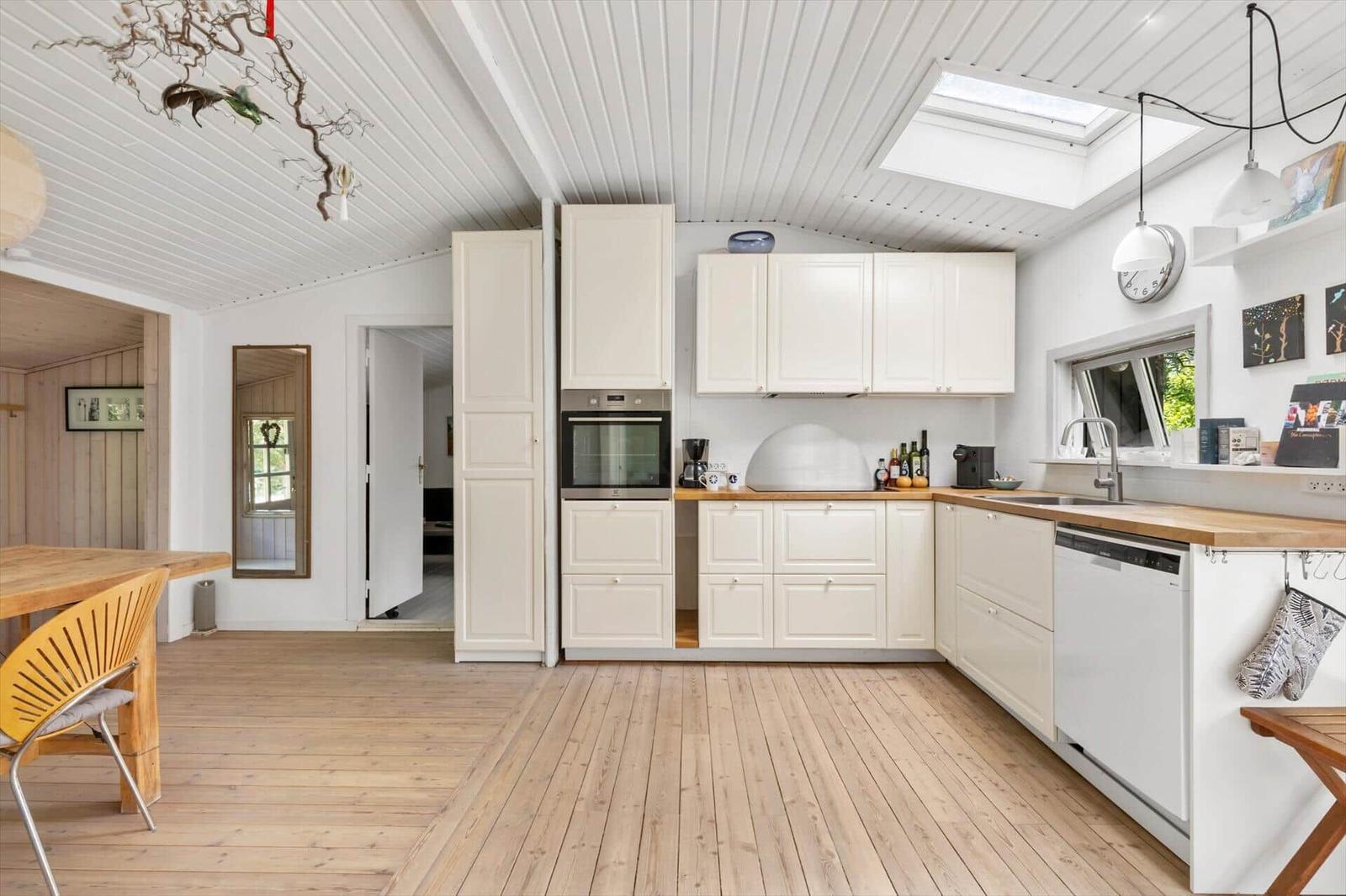 Kitchen with white cabinets, wooden floor, and skylight. Dining table and seating area in foreground.
