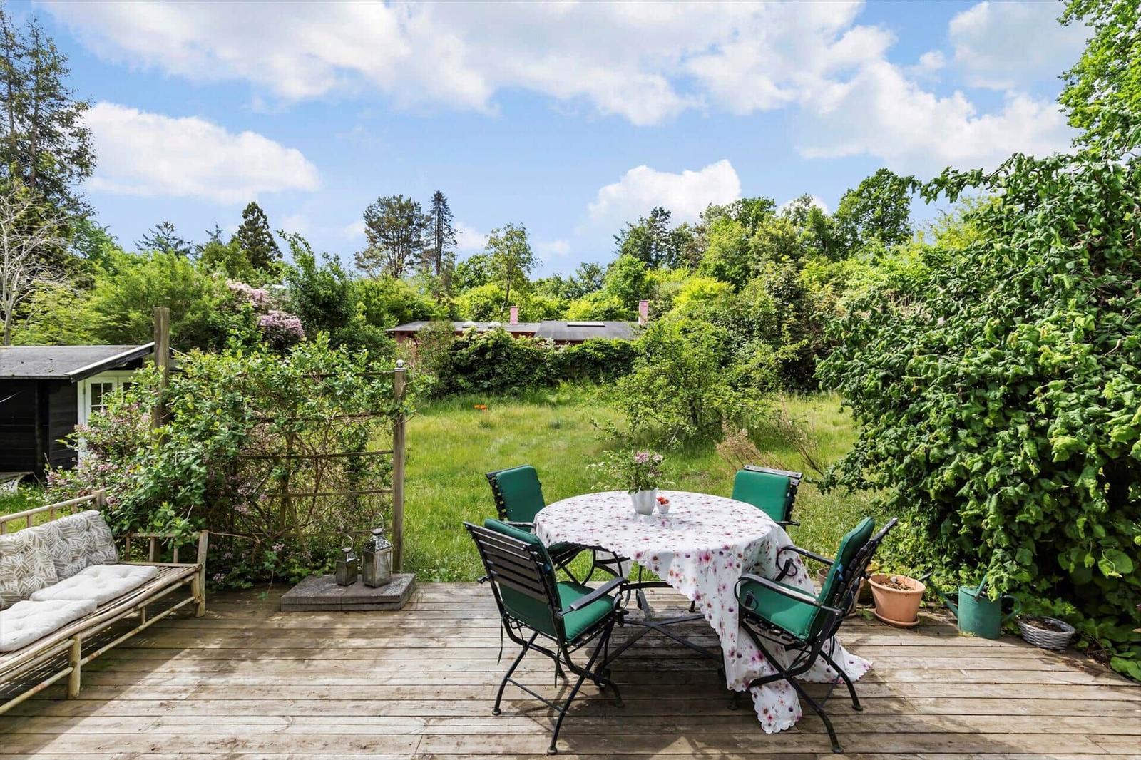Deck with table, chairs, and bench. Green garden and sky in the background.