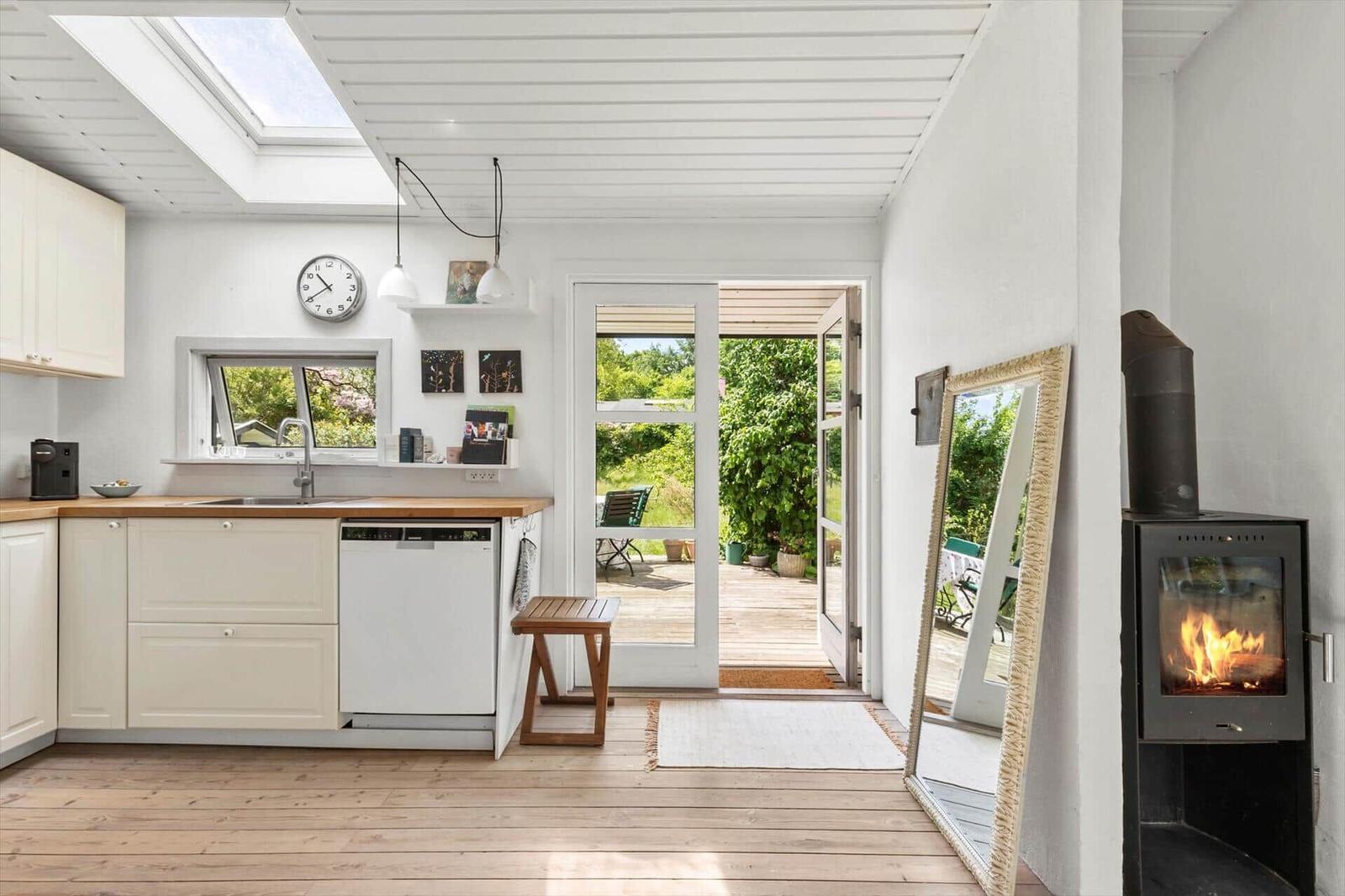 Kitchen with wooden floor, window, door to garden, and wood stove.
