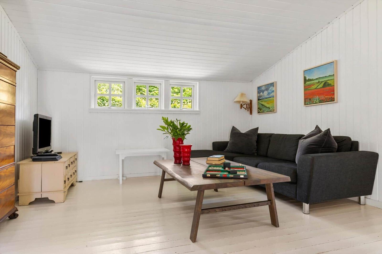 Living room with gray sofa, wooden table, and windows. Wall art and plants.