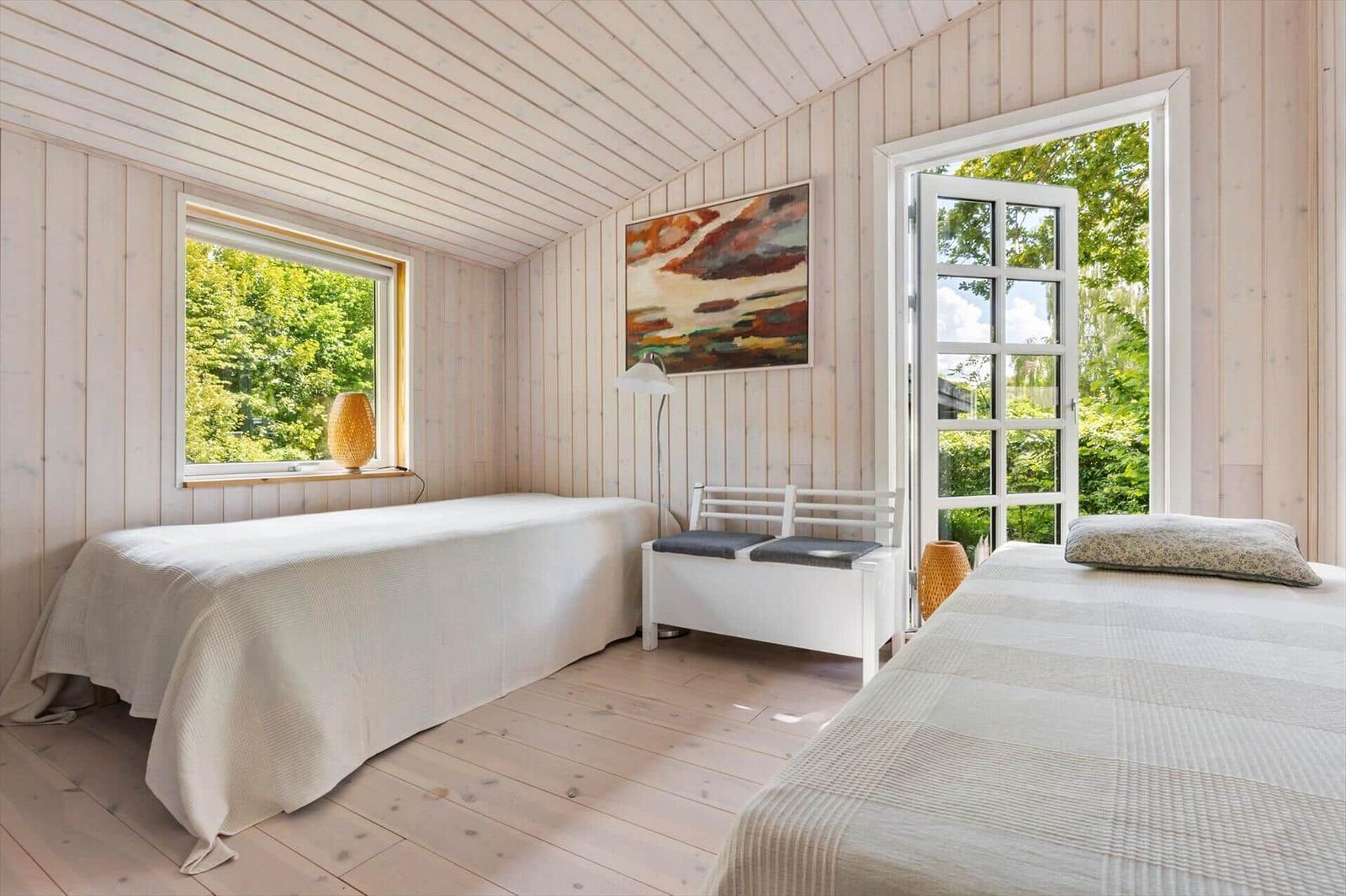 Two beds in a room with wooden walls and windows overlooking greenery.