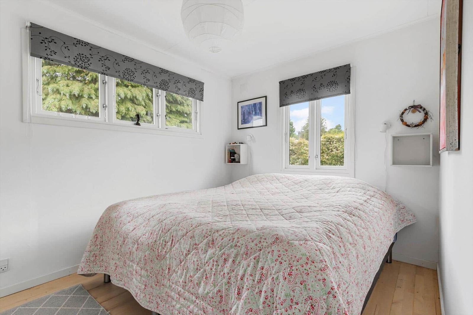 Bedroom with bed, two windows, and wooden floor.