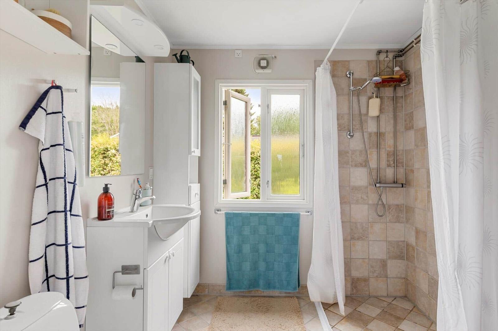 Bathroom with shower, sink, and window. Towel and mirror are present.