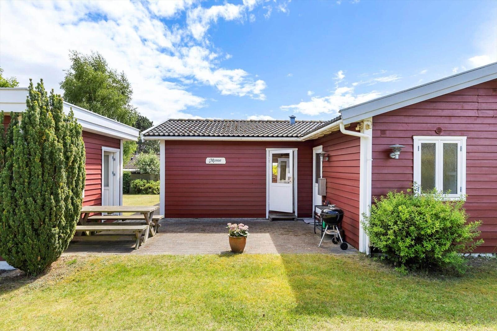 Red wooden house with patio, grill, and seating area in the garden.