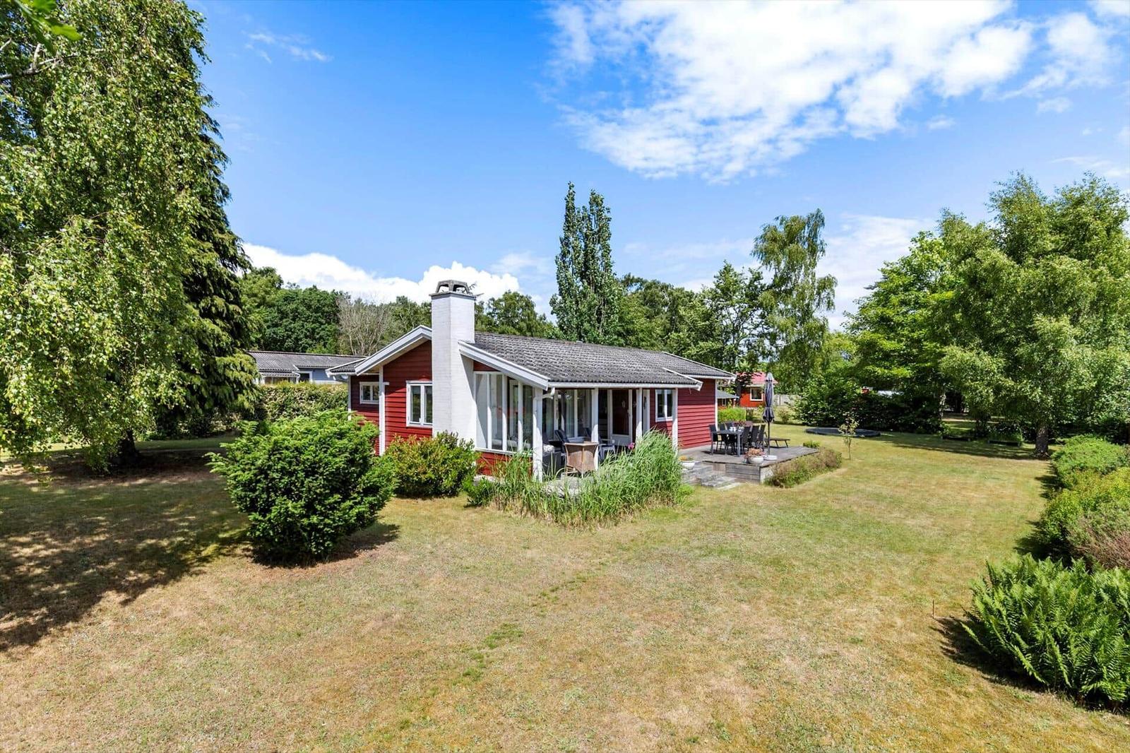 Red house with terrace and garden under blue sky.