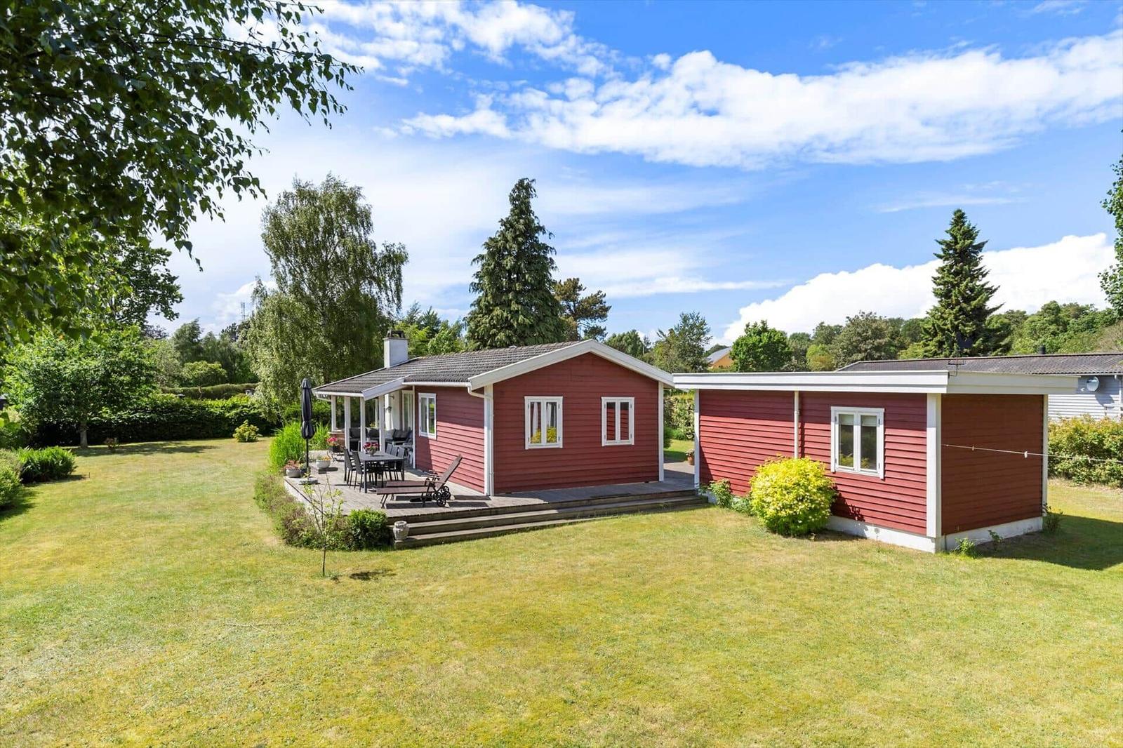 Red wooden house with terrace and garden under blue sky.