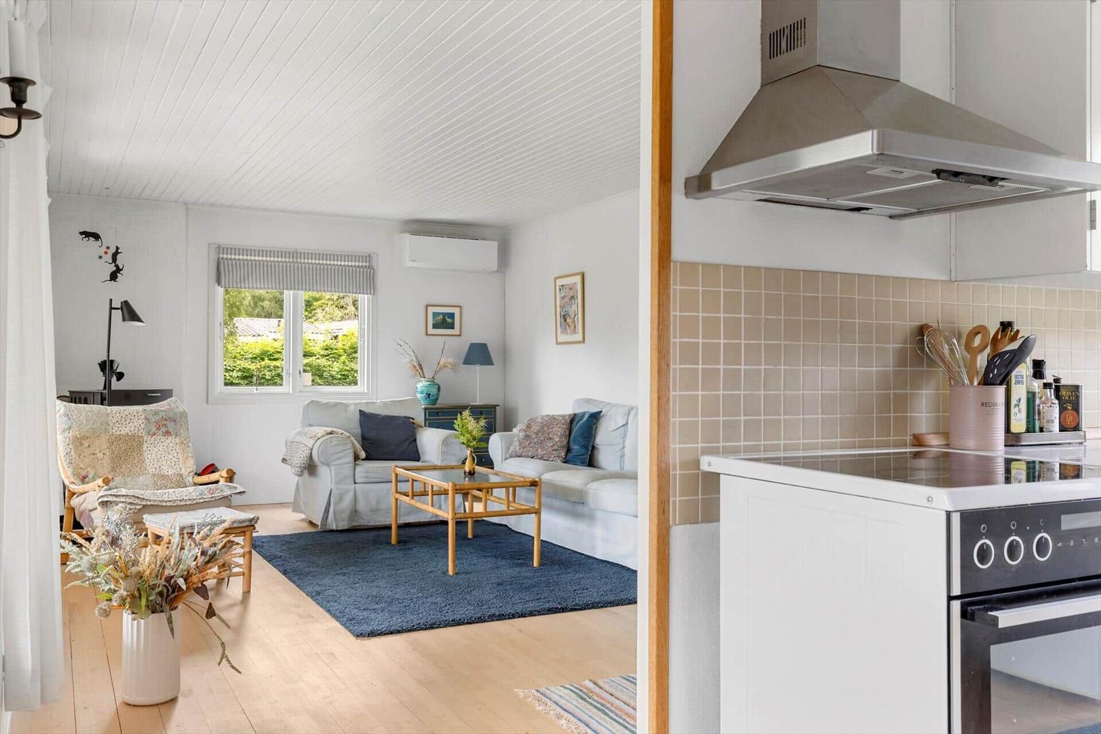 Living room with sofa, coffee table, and window. Kitchen with stove and range hood.