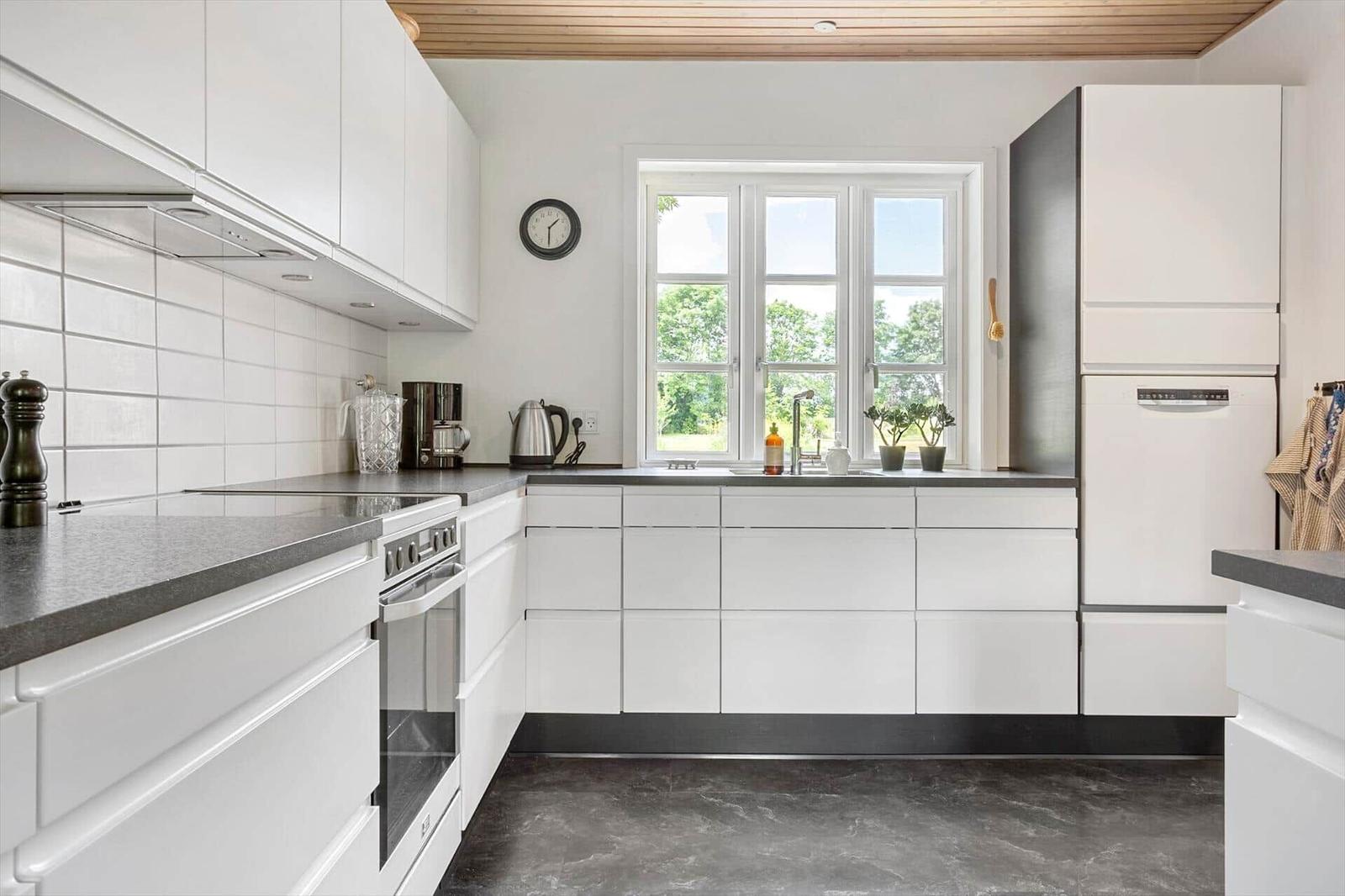 Moderne Küche mit weißen Schränken, dunklem Arbeitsplatz und Fenster mit Blick auf Grün.
