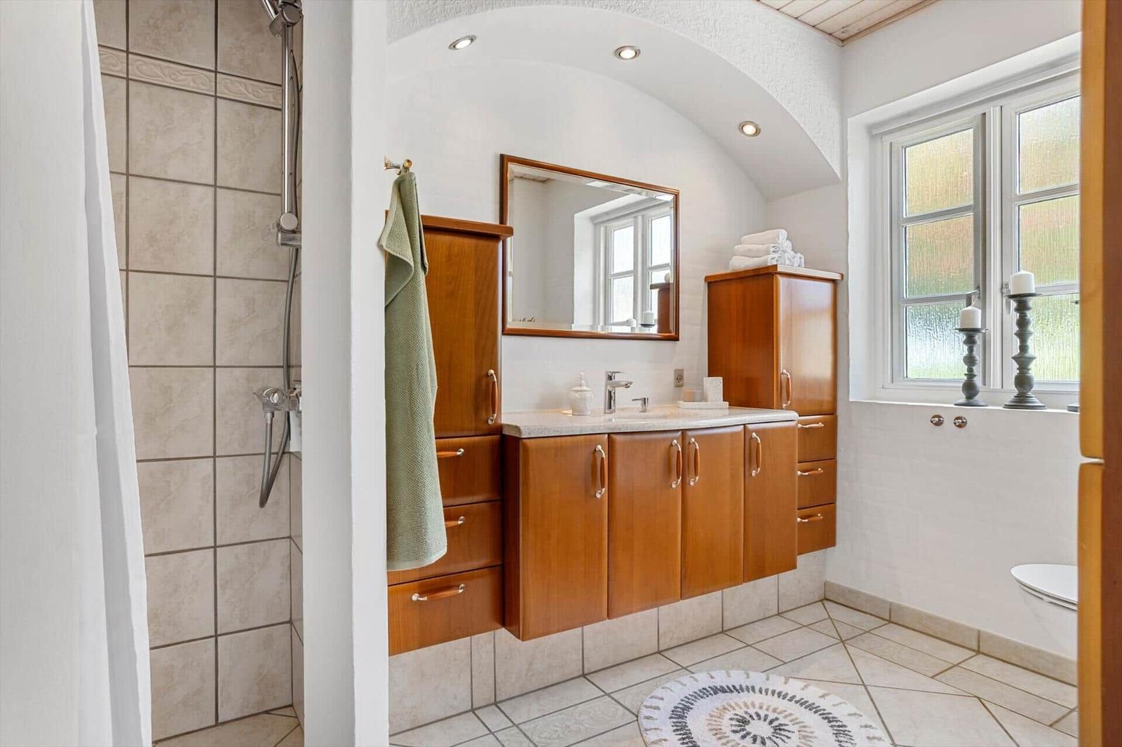 Badezimmer mit Holzschrank, Dusche und Fenster mit Kerzen.
