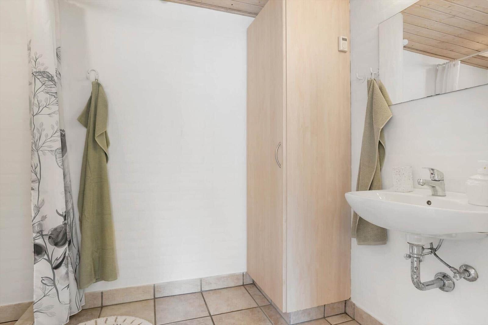 Badezimmer mit Dusche, Waschbecken und Holzschränkchen.