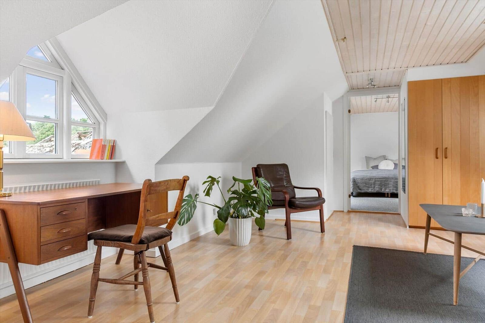 Dachgeschosszimmer mit Schreibtisch, Sessel und Blick auf Schlafzimmer.