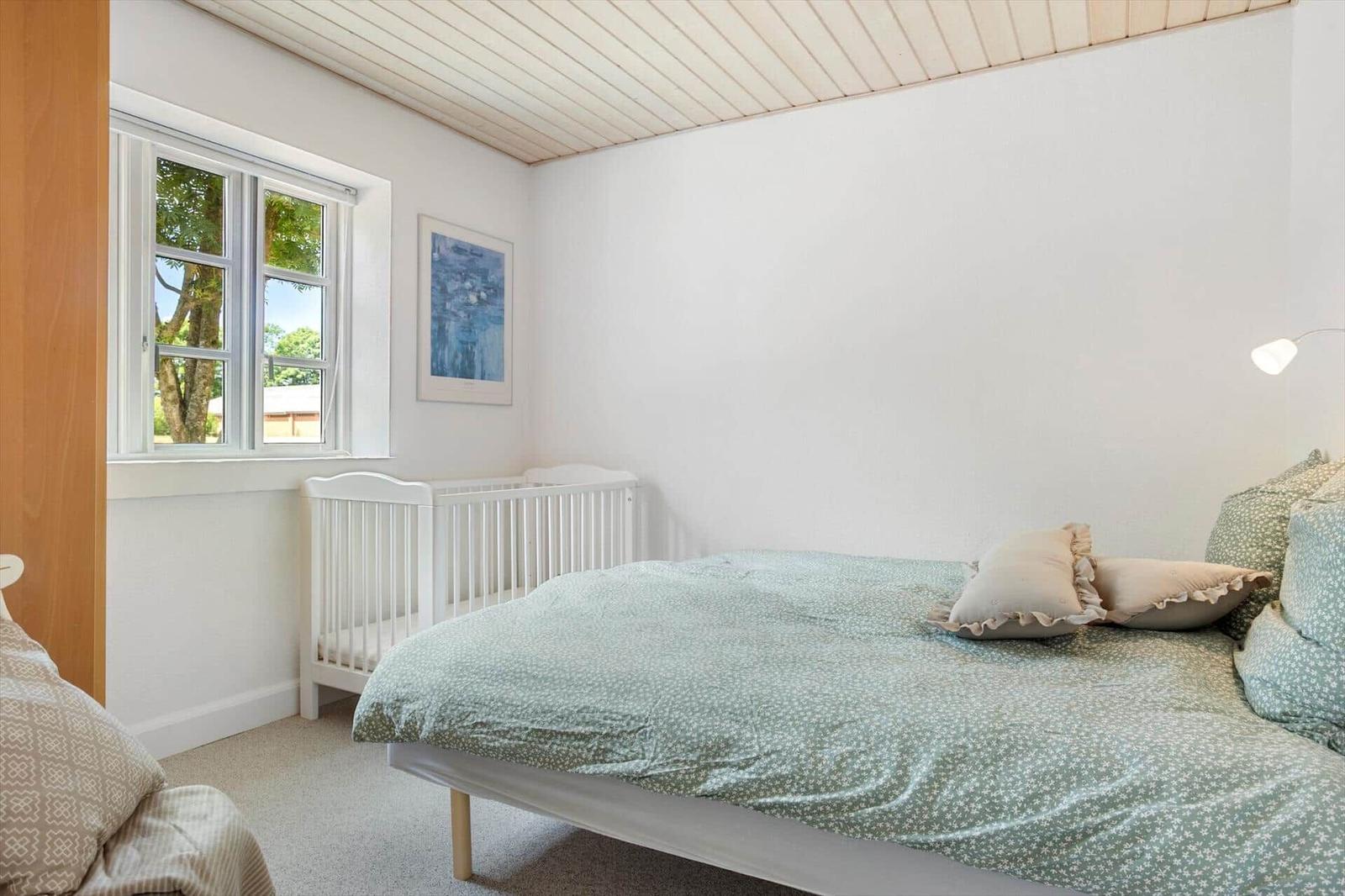 Schlafzimmer mit Bett, Kinderbett und Fenster mit Blick auf Bäume.