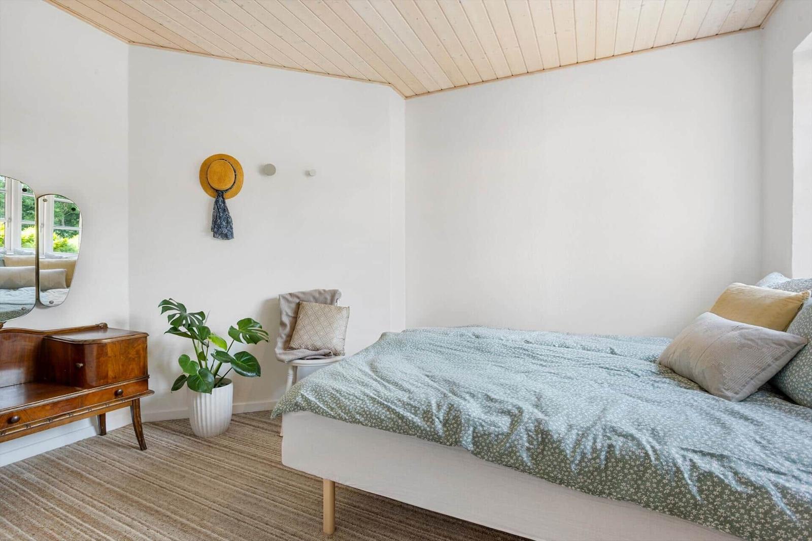Schlafzimmer mit Bett, Holzdecke, Pflanze und Spiegel.