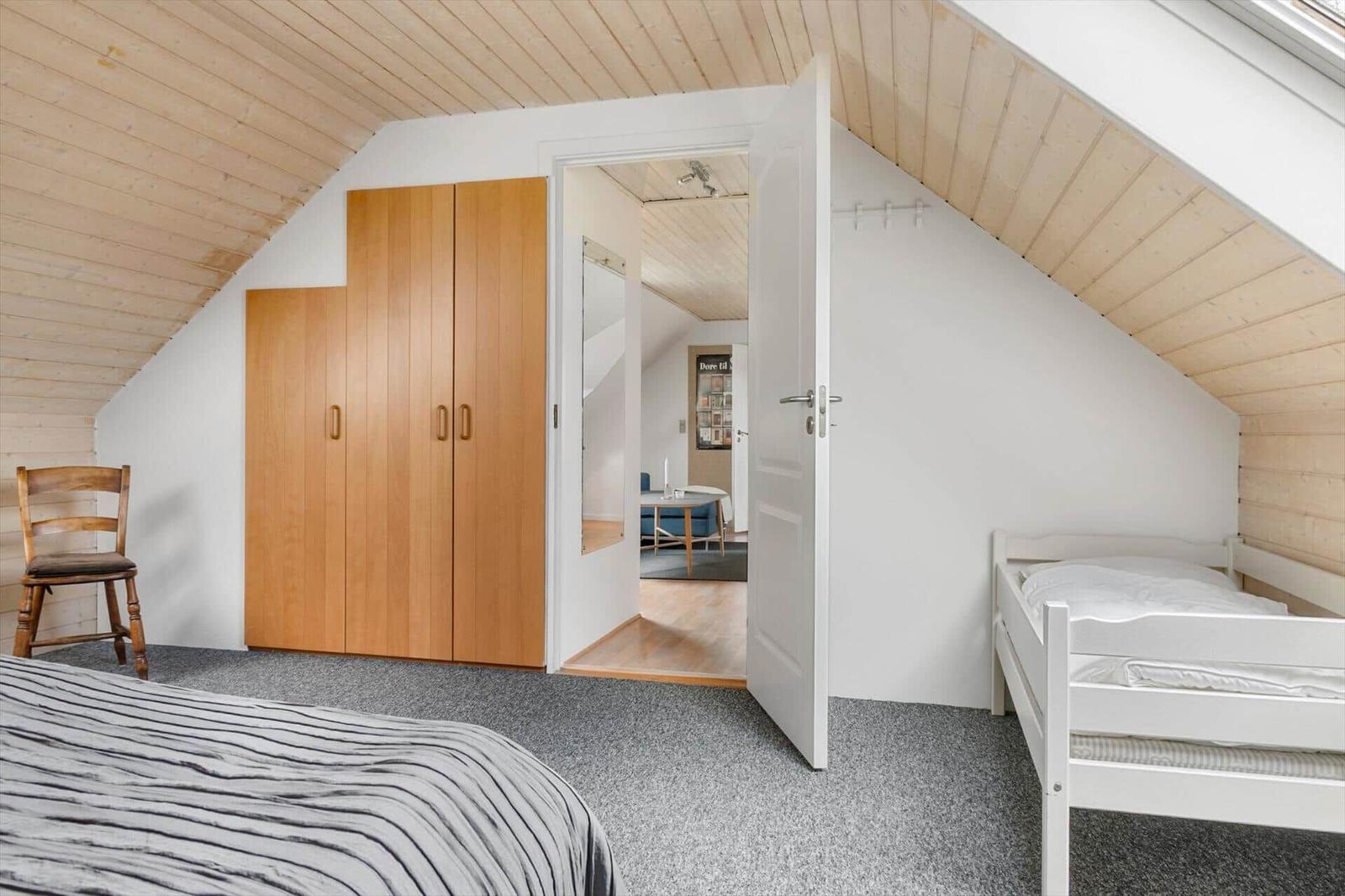 Schlafzimmer mit Dachschräge, Kleiderschrank und Bett. Tür führt in Wohnbereich.