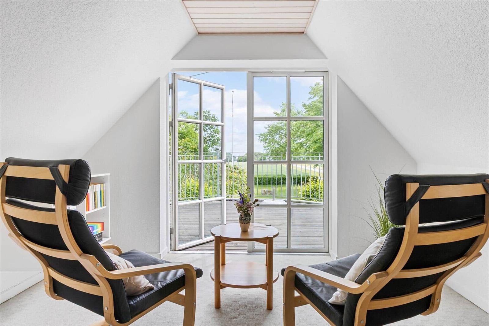 Zwei schwarze Sessel und ein Tisch stehen vor einer Glastür mit Blick auf Balkon und Garten.