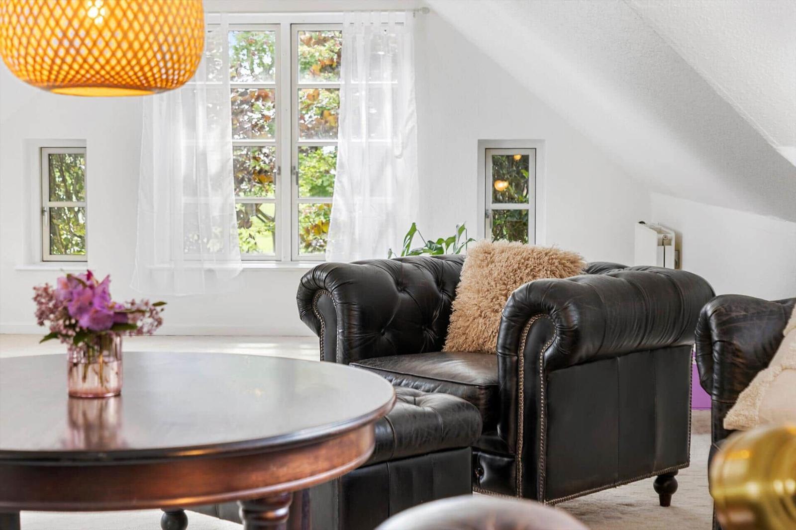 Wohnzimmer mit schwarzem Ledersofa, runden Tisch und Fenster mit Blick auf Grün.