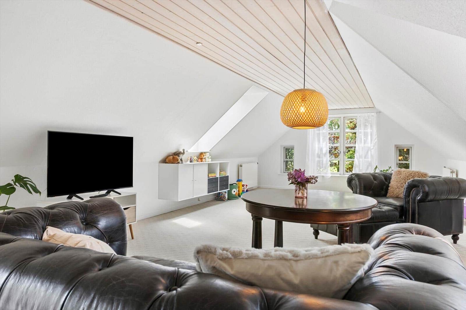 Wohnraum mit schwarzem Ledersofa, runden Tisch und TV an der Wand.
