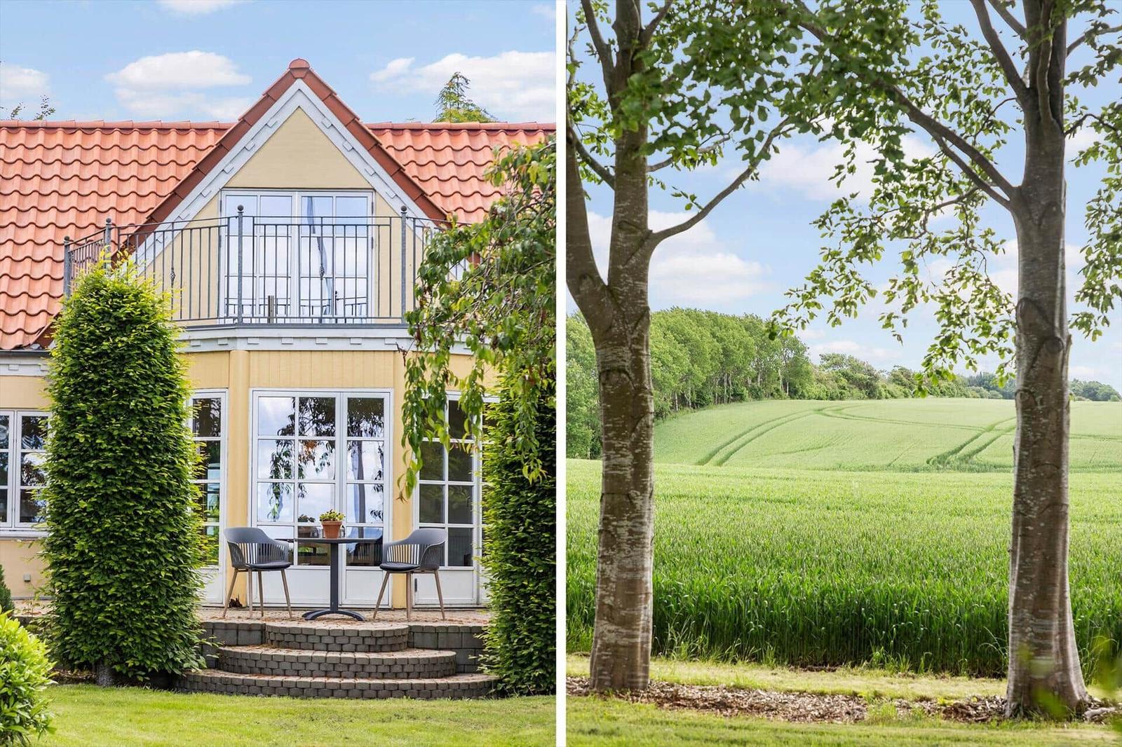 Ferienhaus mit Balkon und Terrasse. Grüne Wiese und Bäume im Hintergrund.