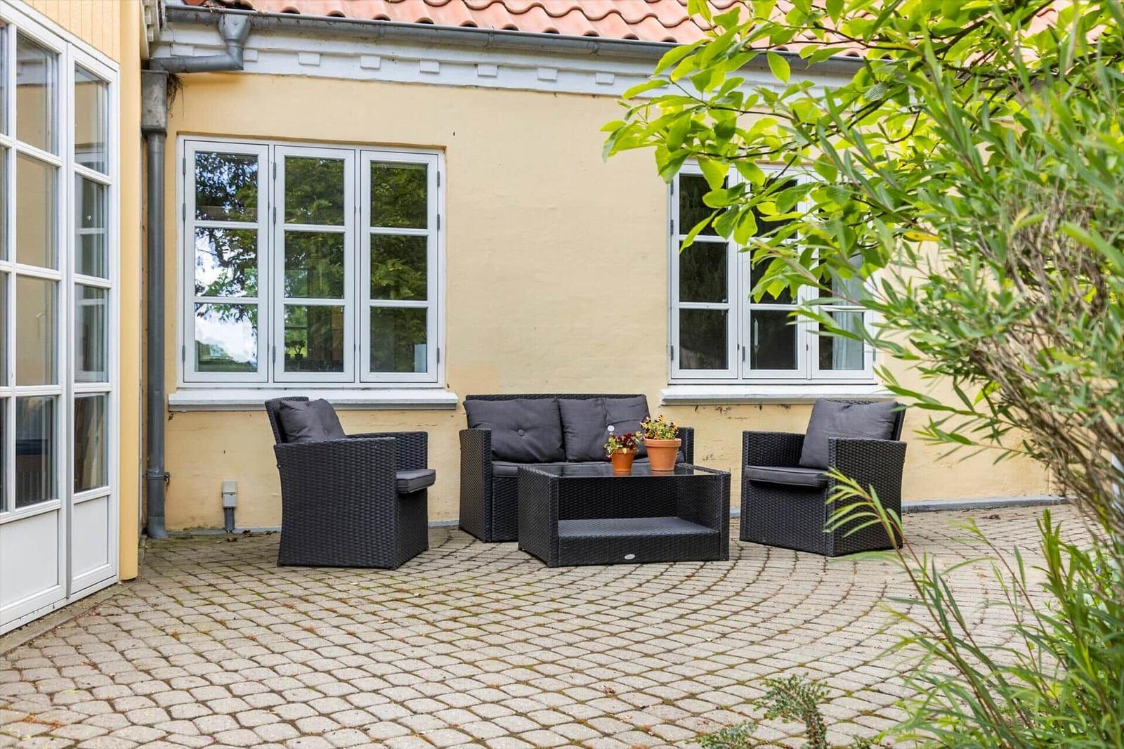 Terrasse mit Sitzgruppe, Pflanzen und gelbem Haus mit Fenstern.