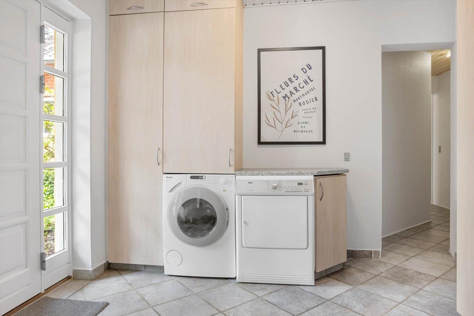 Wäscherei mit Waschmaschine und Trockner, Holzschränke und Wandbild.