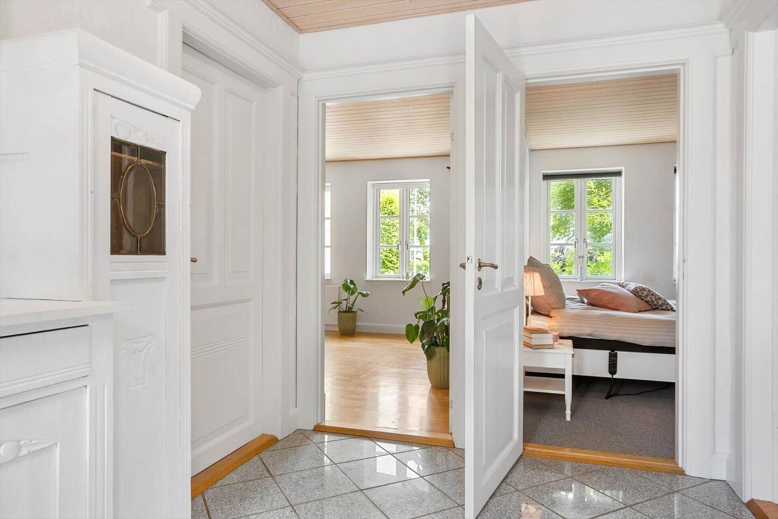 Hausflur mit Blick in Schlafzimmer und Wohnbereich mit Holzboden und Fenstern.