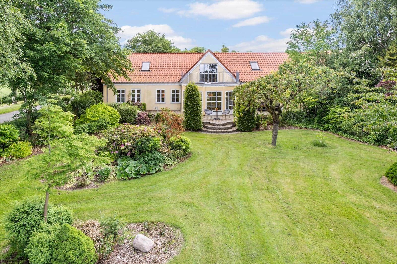Haus mit rotem Dach und großem Garten. Terrasse mit Tisch und Stühlen.