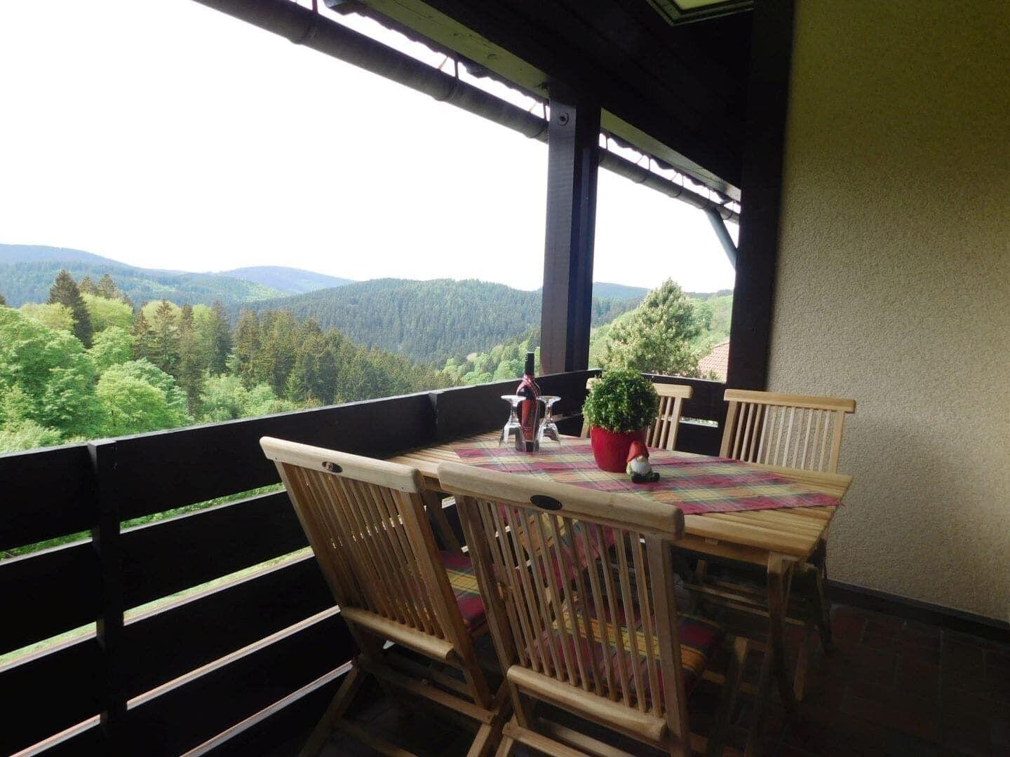 Terrasse mit Holztisch und Stühlen, Blick auf Wald und Berge.