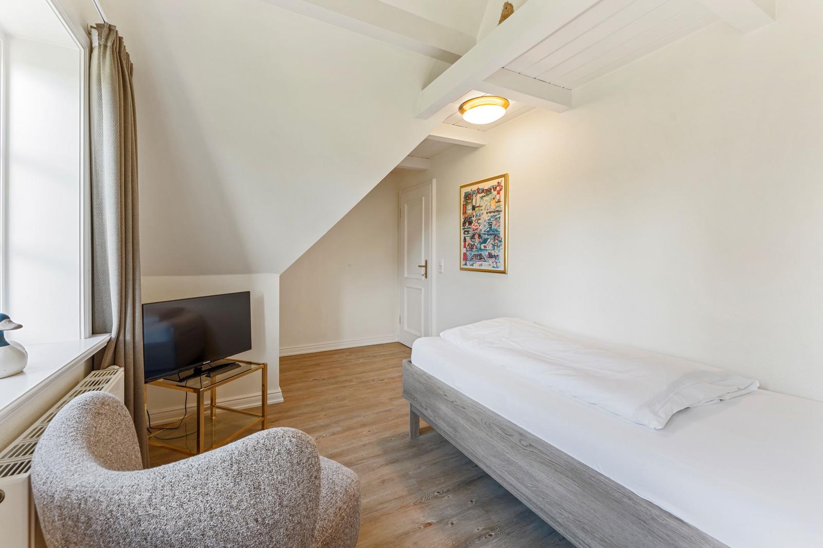 Zimmer mit Bett, TV und Sessel unter schrägem Dach