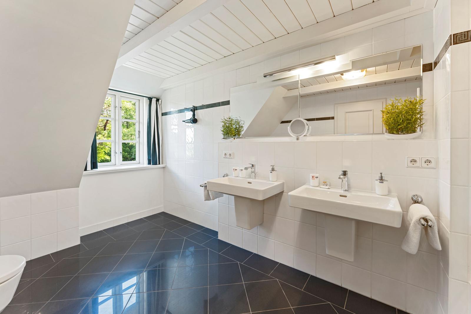 Badezimmer mit zwei Waschbecken, Spiegel und Fenster mit Blick auf Grün.