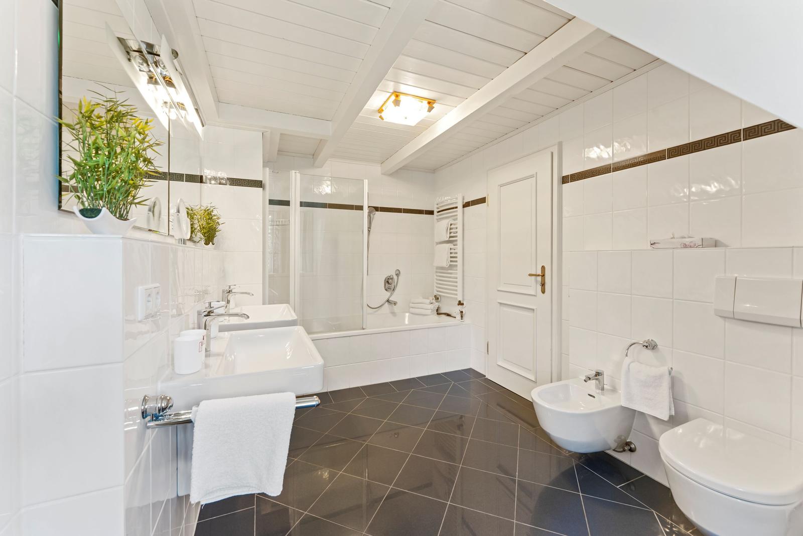 Badezimmer mit Dusche, Waschbecken und Toilette. Weiße Fliesen und dunkler Boden.