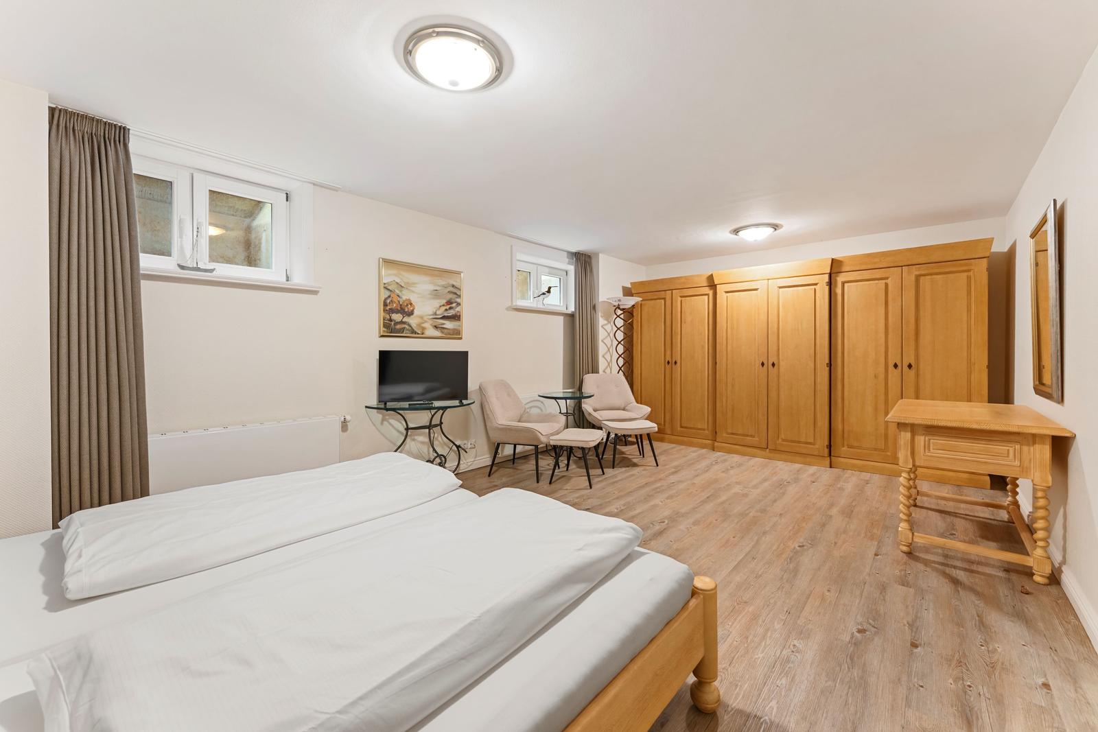 Schlafzimmer mit Bett, Schränken, TV und Sitzgelegenheit.