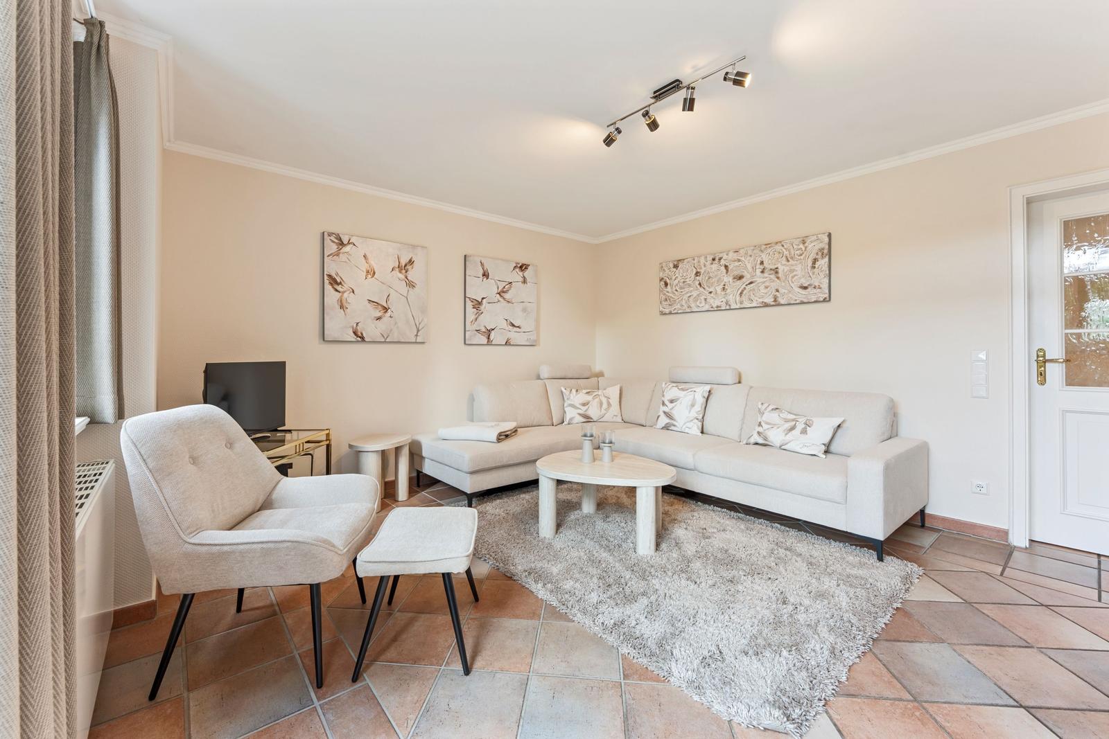 Wohnzimmer mit Sofa, Sessel und Tisch. Wandbilder und Teppich sind vorhanden.