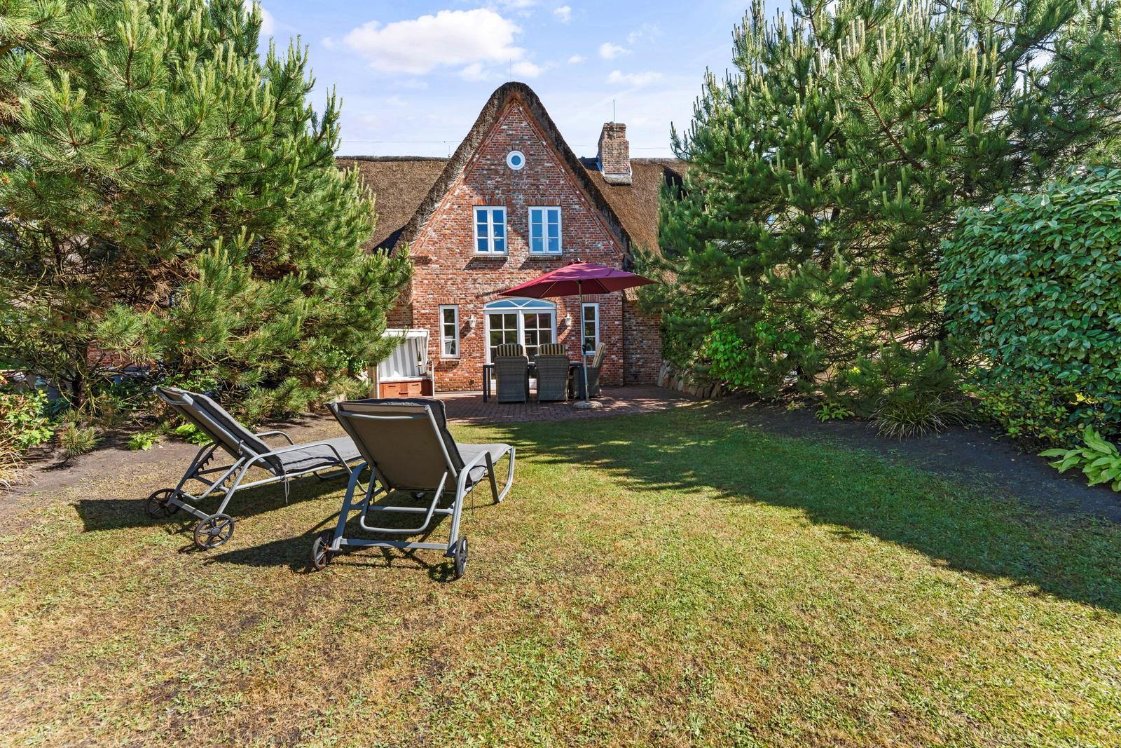 Haus mit Garten, Sonnenliegen und Terrasse mit Tisch und Stühlen.