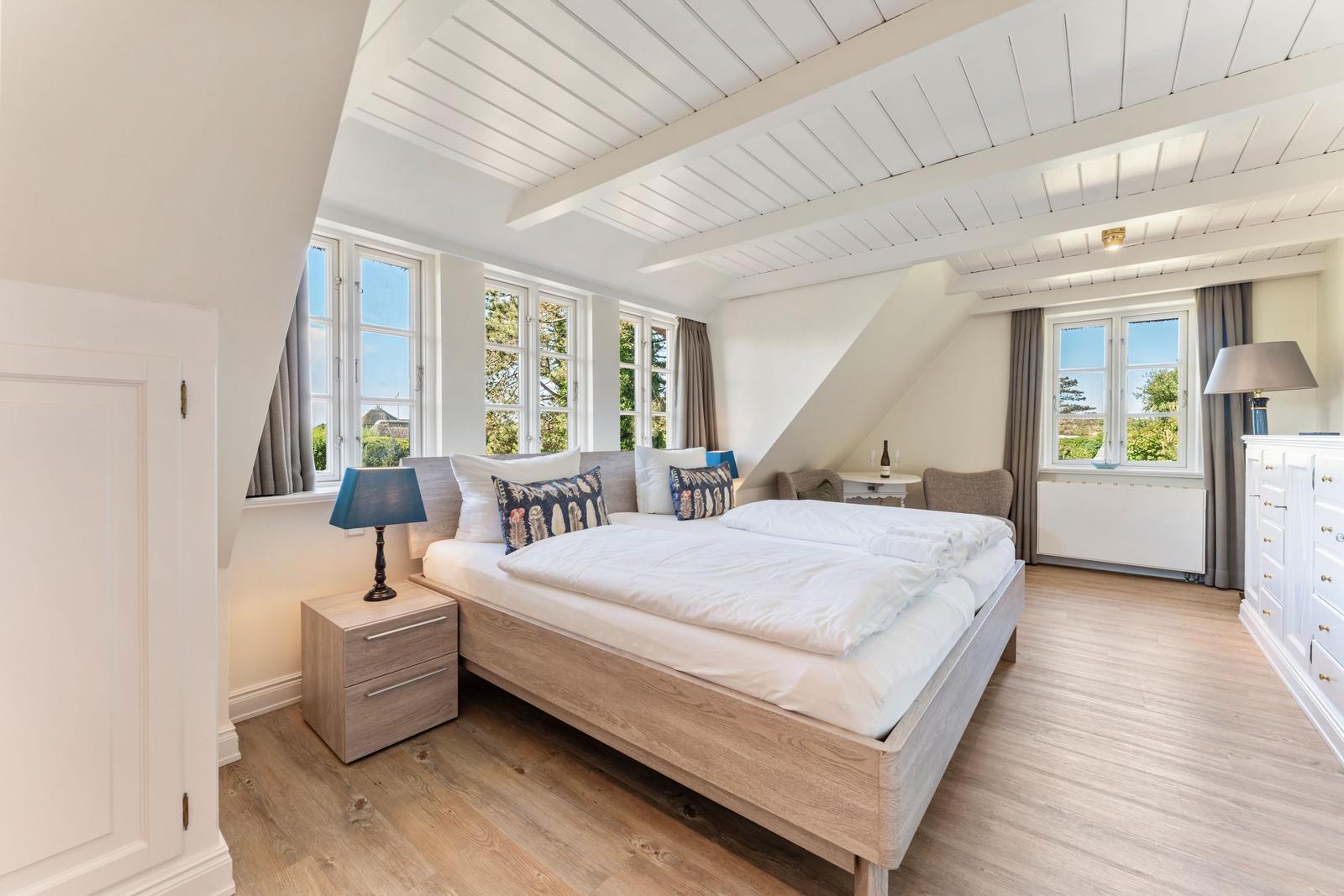 Schlafzimmer mit Doppelbett, Fenstern und Holzboden.