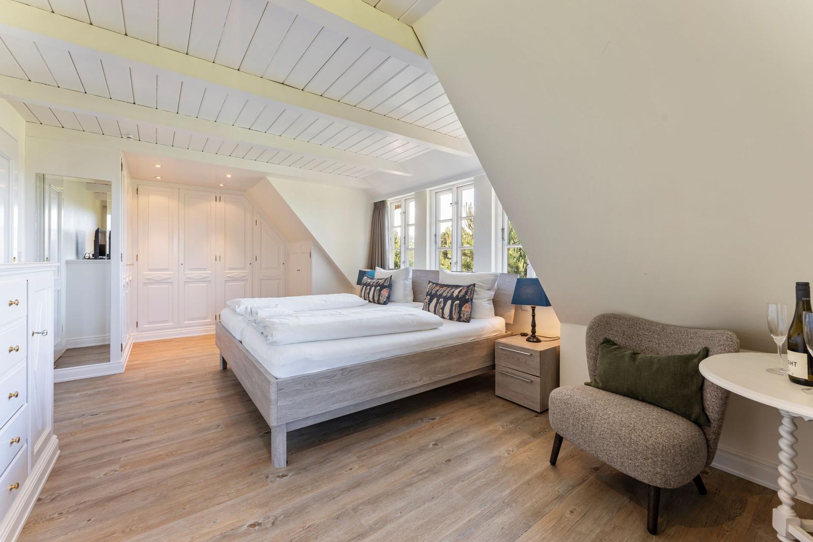 Schlafzimmer mit Dachschräge, Bett, Nachttisch, Sessel und Fenster