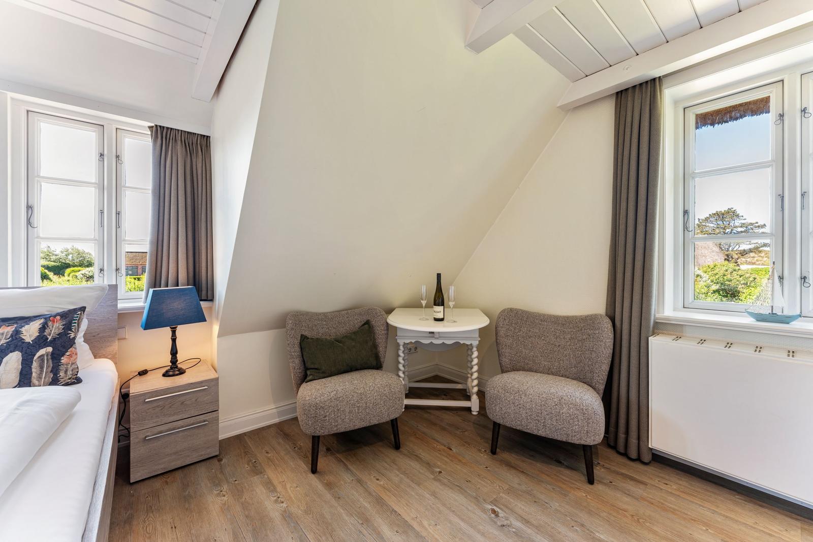 Zimmer mit zwei Sesseln, Tisch, Bett und Fenstern mit Blick.