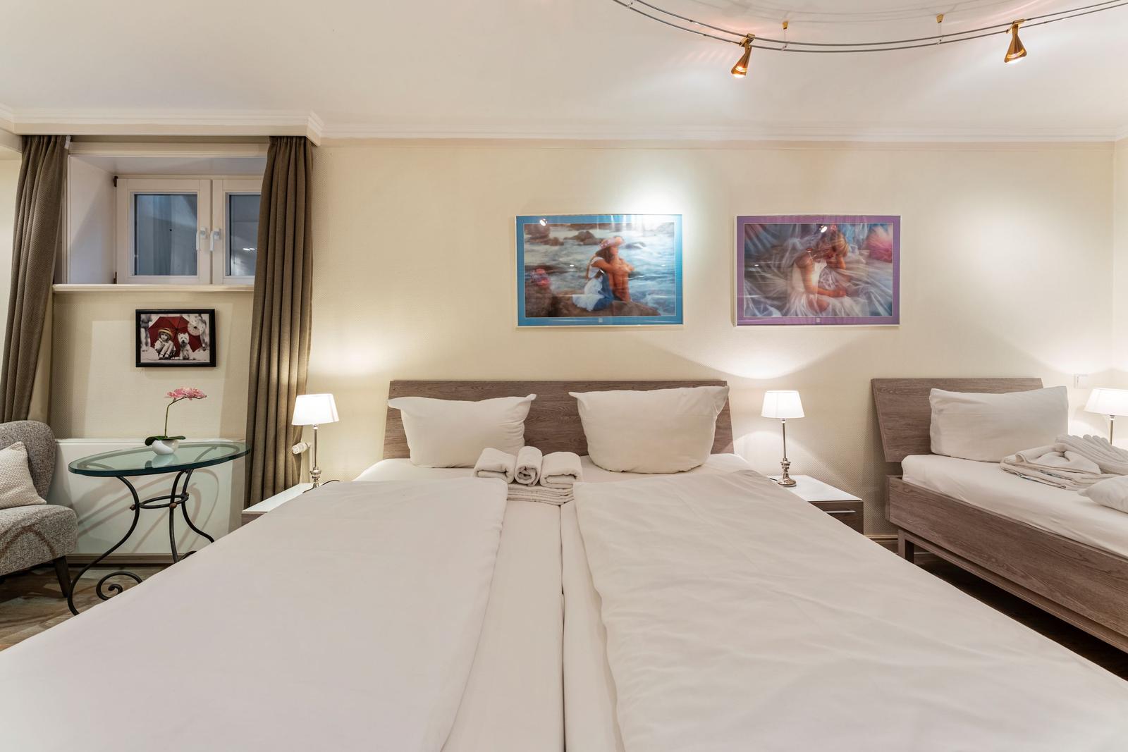 Zimmer mit zwei Betten, Wandbildern und Fenster mit Vorhängen.