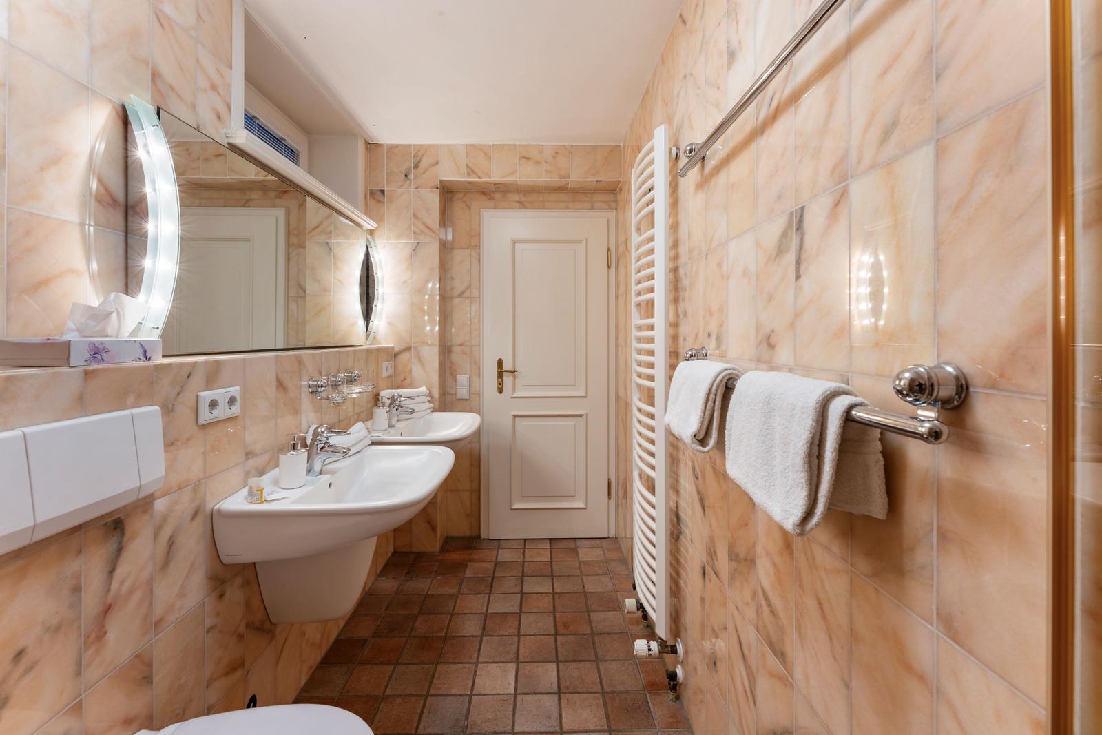 Badezimmer mit Marmortapete, zwei Waschbecken und Handtuchhalter