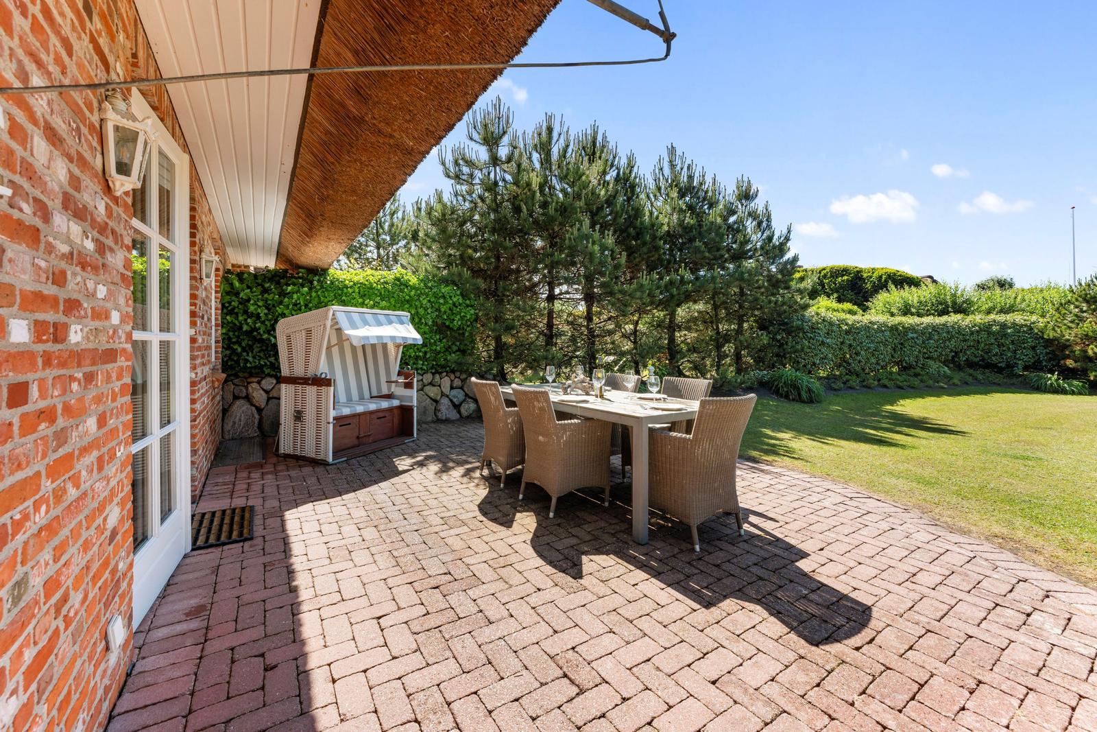 Terrasse mit Esstisch, Stühlen und Strandkorb. Hinterhof mit Rasen und Bäumen.