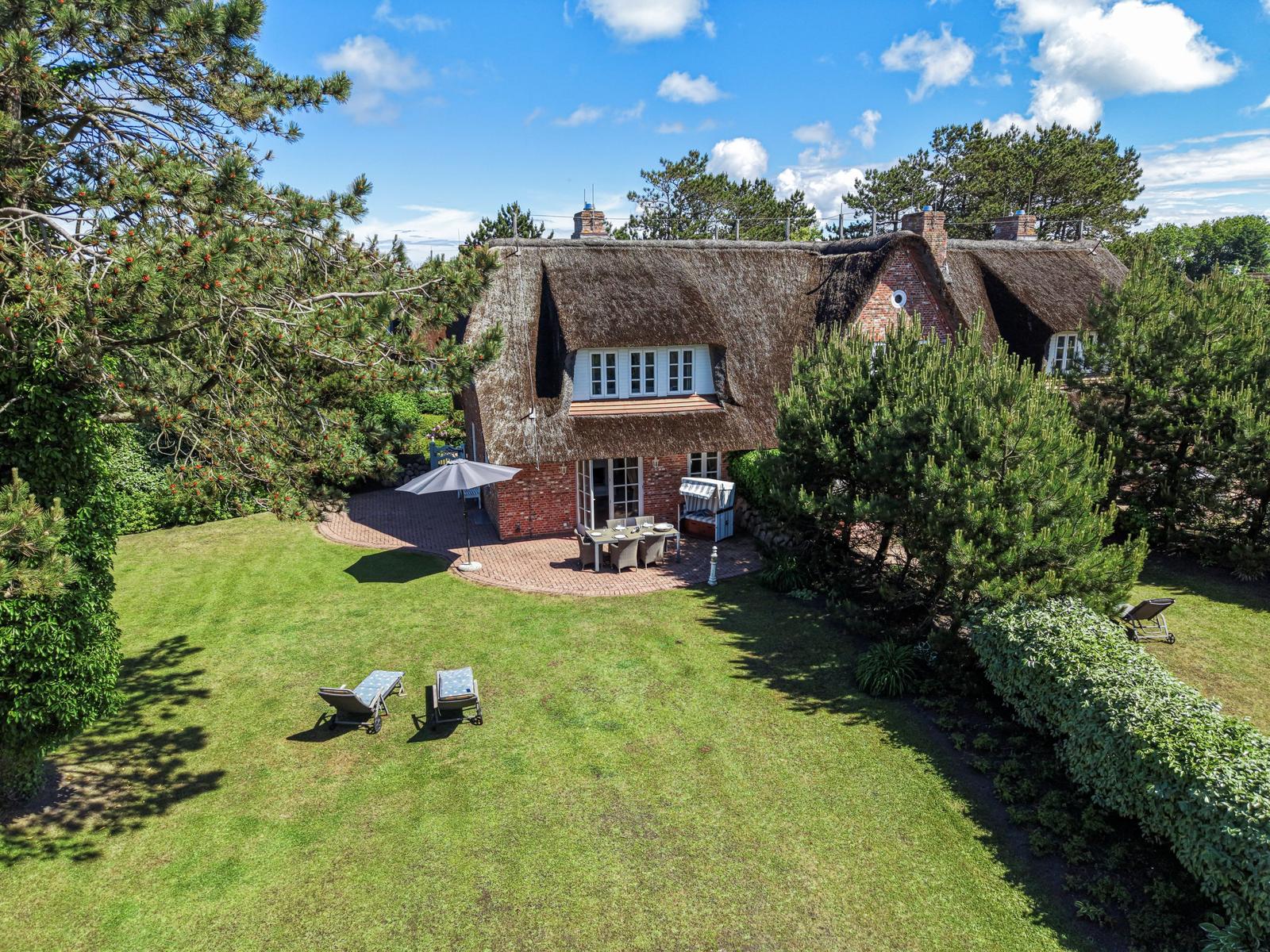Haus mit Strohdach, Terrasse und Garten mit Liegestühlen.
