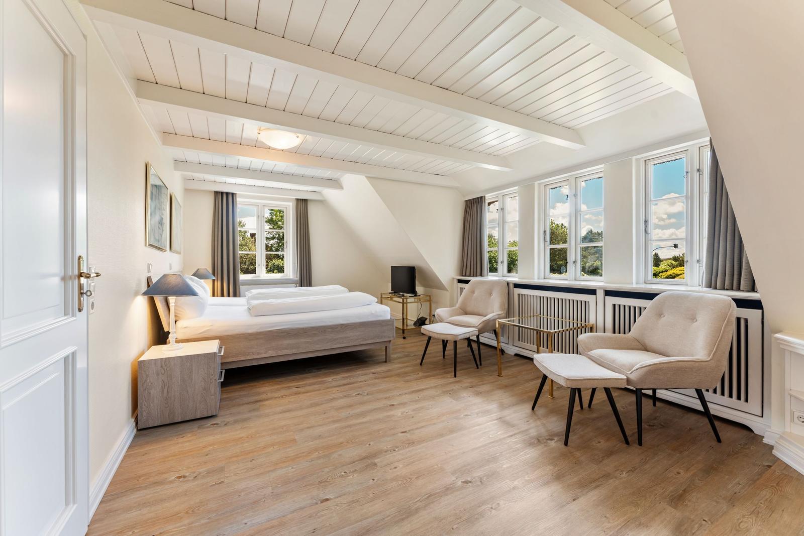 Schlafzimmer mit Dachschräge, Bett, zwei Sessel und Fenstern mit Blick.