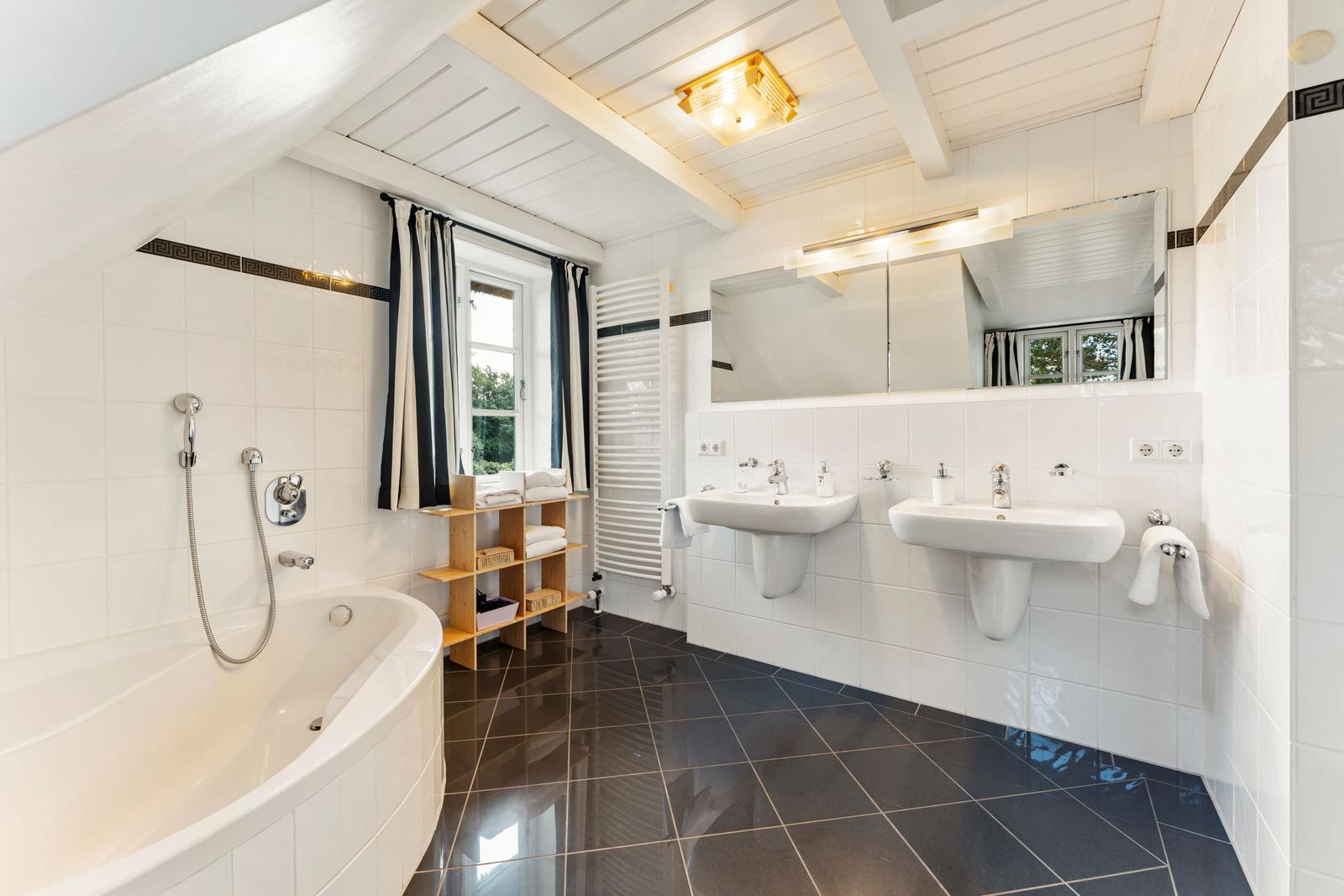 Bad mit Badewanne, zwei Waschbecken und Fenster mit Vorhängen.