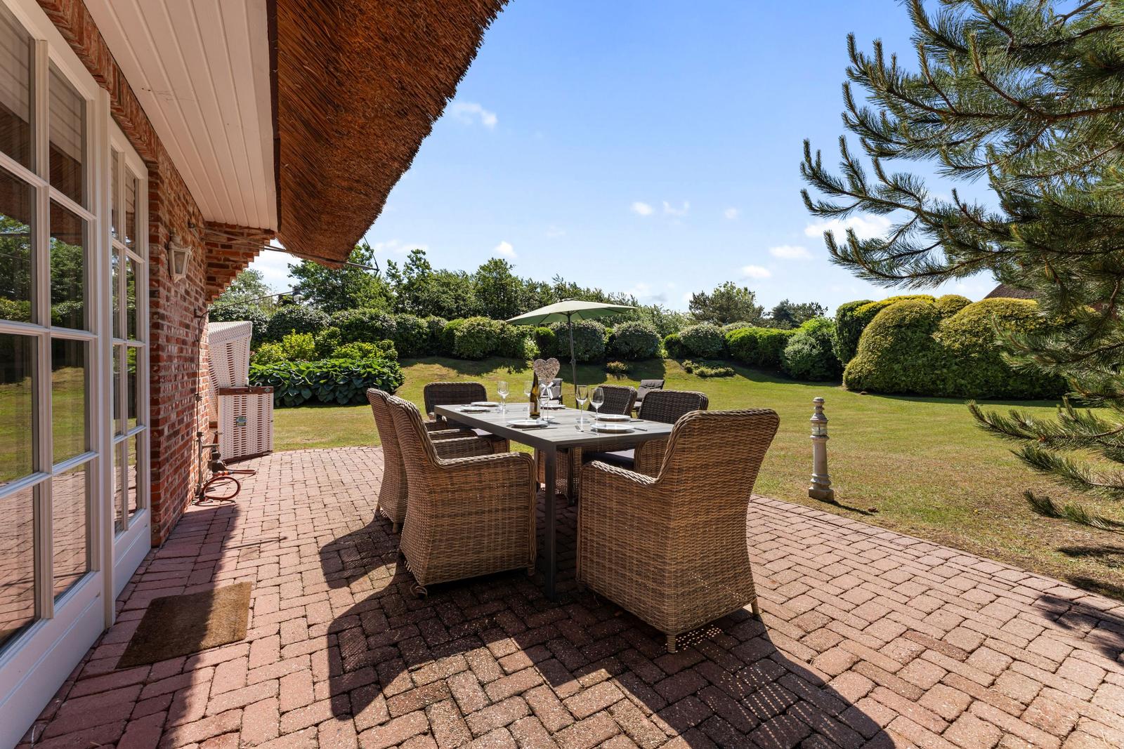 Terrasse mit Esstisch und Stühlen, Blick auf grünen Garten mit Hecken und Baum.
